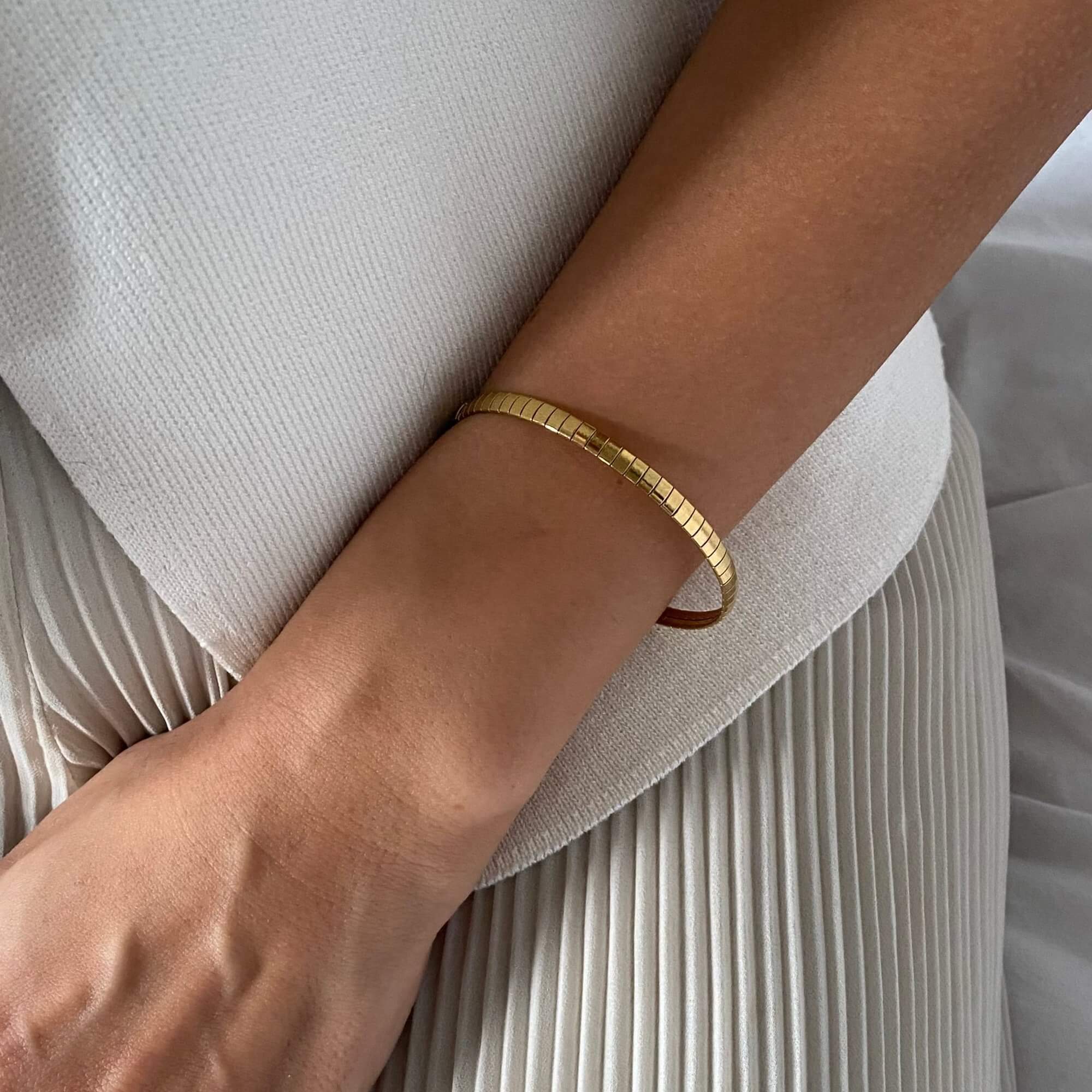 The KenyaB 18K gold-plated flat gold bracelet (4mm) by Kampy Designs, elegantly worn to highlight its sleek and minimalist design.