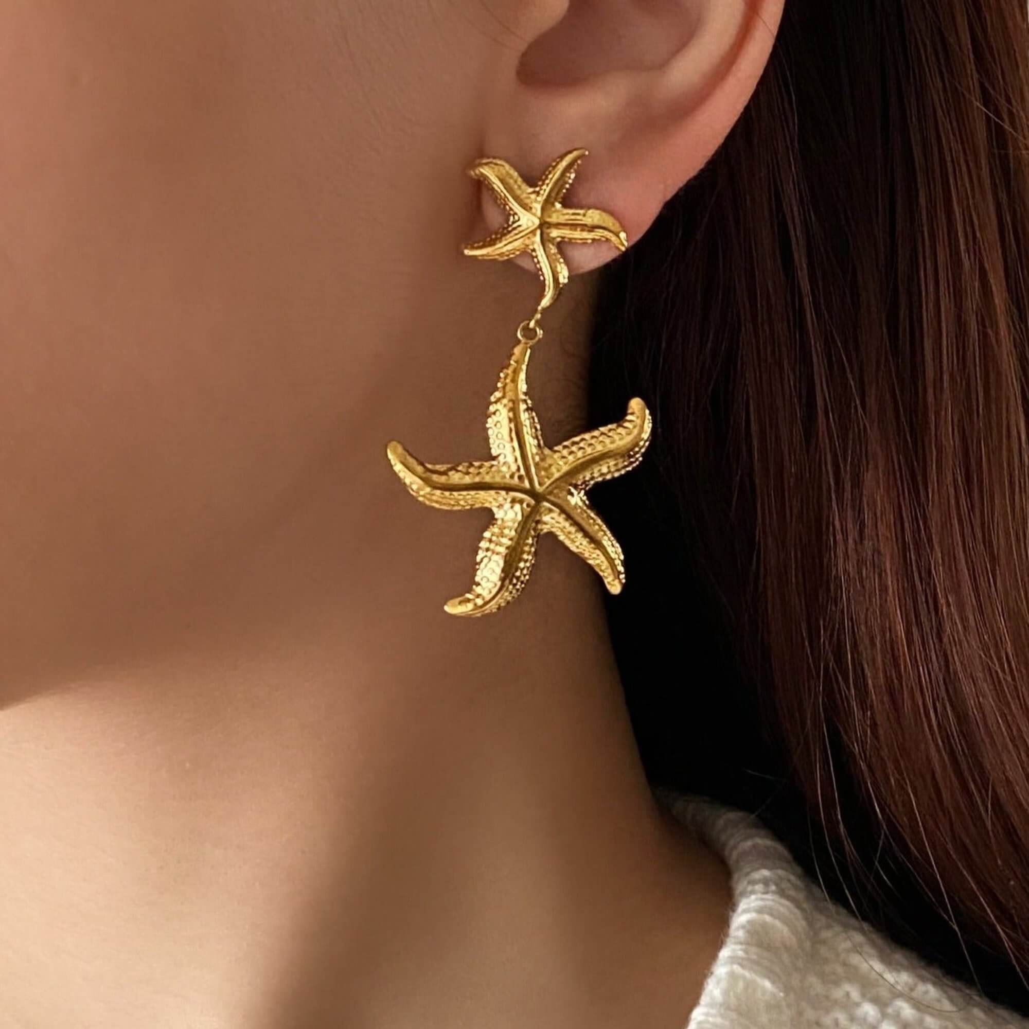 The KetaroE 18K gold-plated starfish dangle earrings by Kampy Designs, stylishly paired with other accessories for a beach-inspired, sophisticated look.