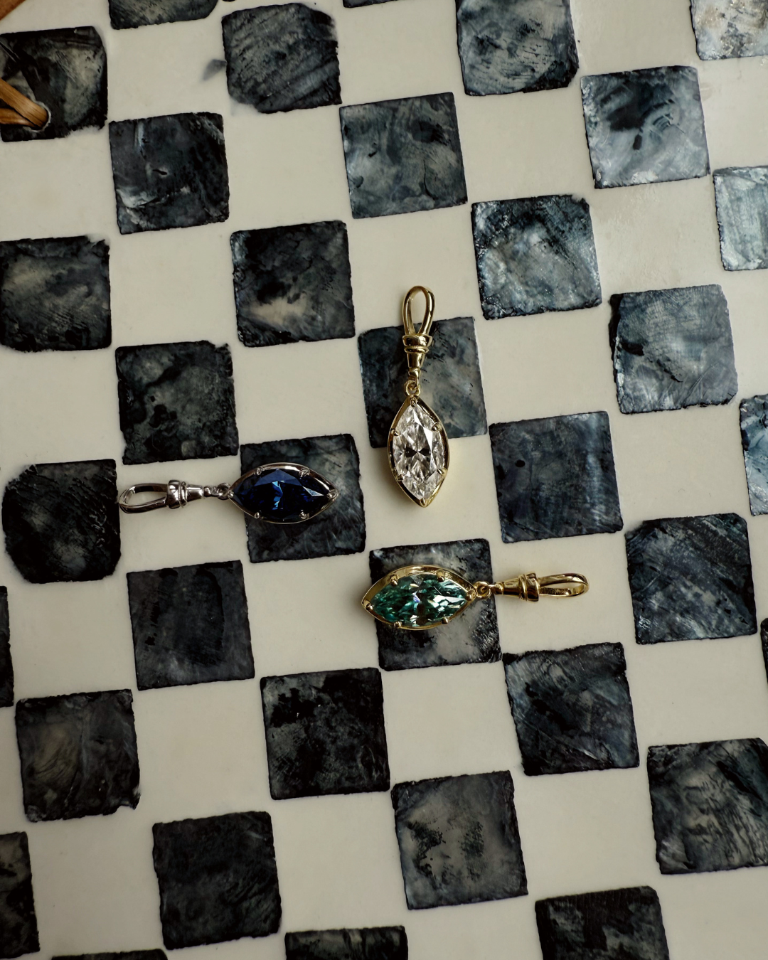 Marquise moissanite pendant charms in green, white, and midnight blue displayed on patterned surface.