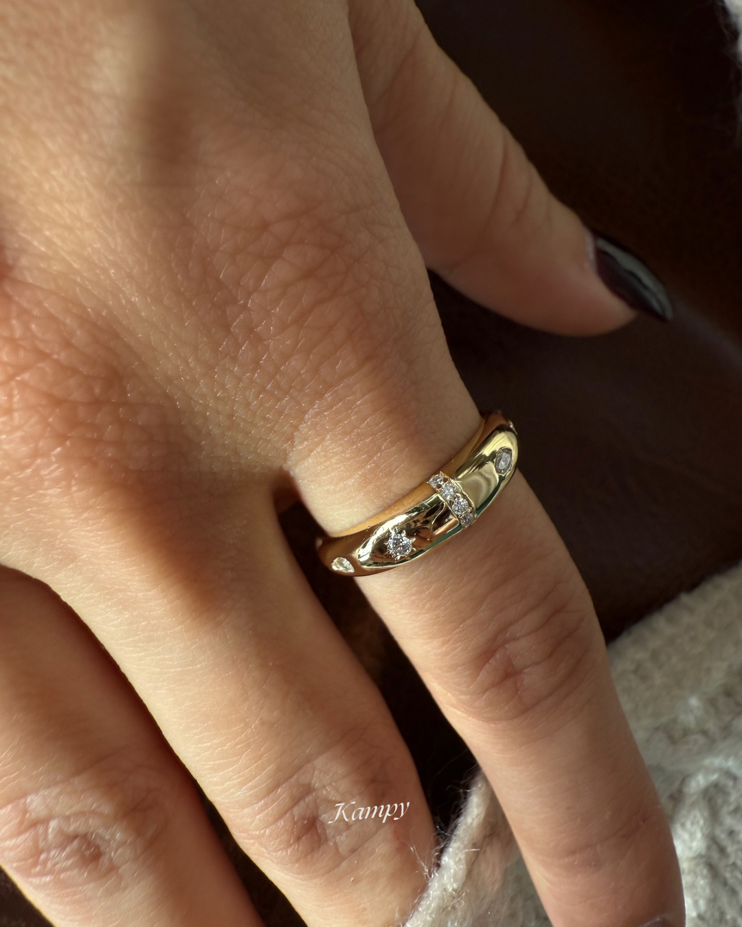 Gold ring with a moissanite accents on a finger, brand 'Kampy' visible