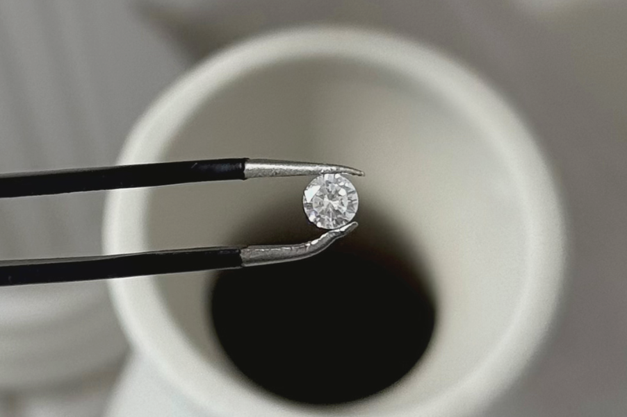 Diamond held by tweezers over a white vase with promotional text for moissanite jewelry.
