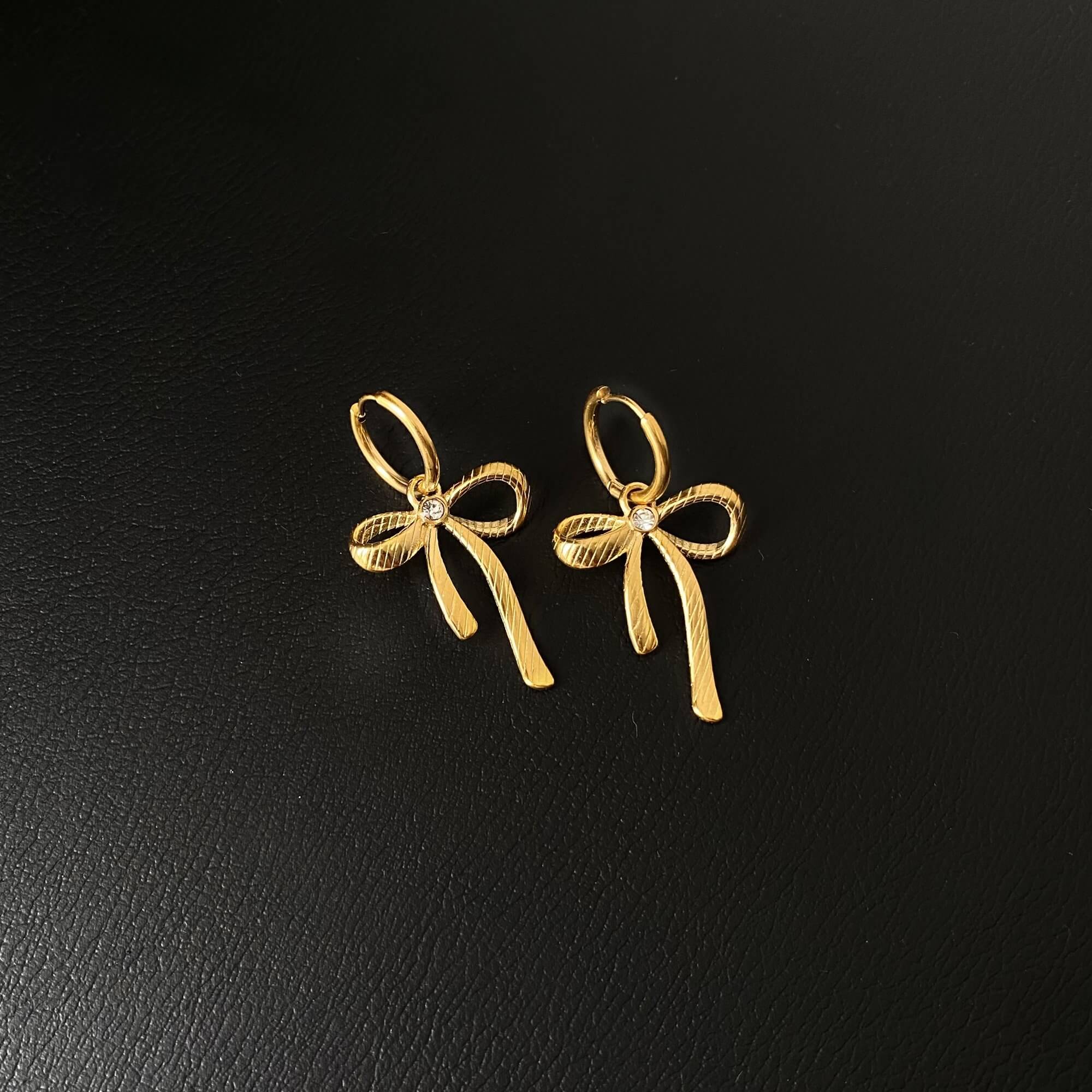Flat lay of KrissaE dainty bow dangle earrings by Kampy Designs, featuring the symmetrical bows and slim dangling threads.