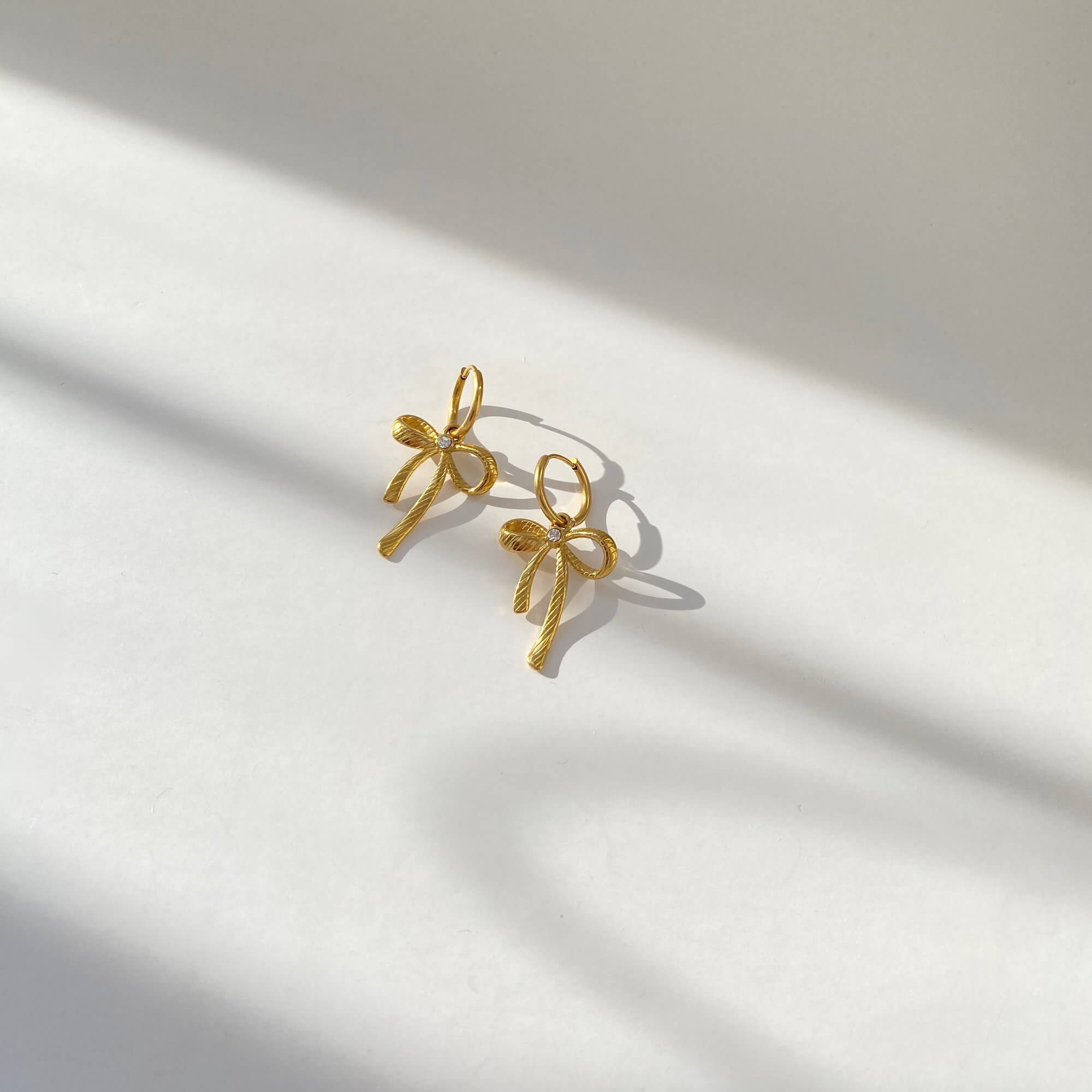 Top-down view of KrissaE dainty bow dangle earrings by Kampy Designs, emphasizing the looped bow tops and slender dangles.