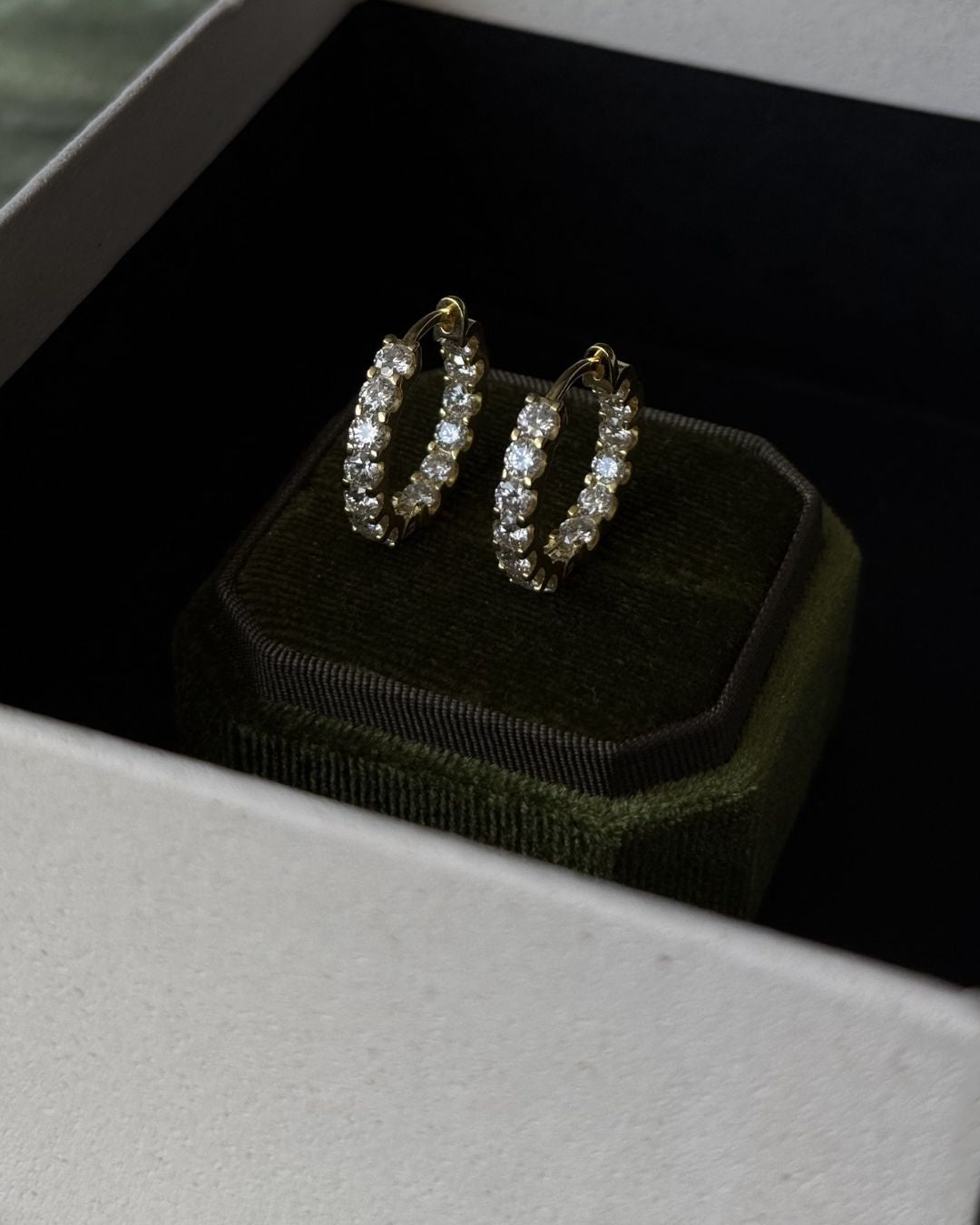 Pair of gold moissanite huggie hoop earrings displayed on a black background with sparkling round stones.