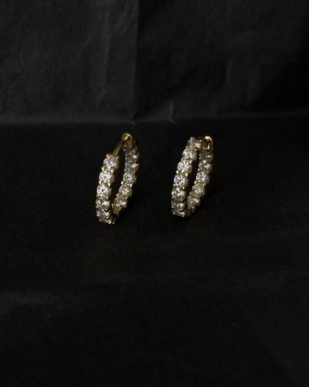 Pair of gold moissanite huggie hoop earrings displayed on a black background with sparkling round stones.