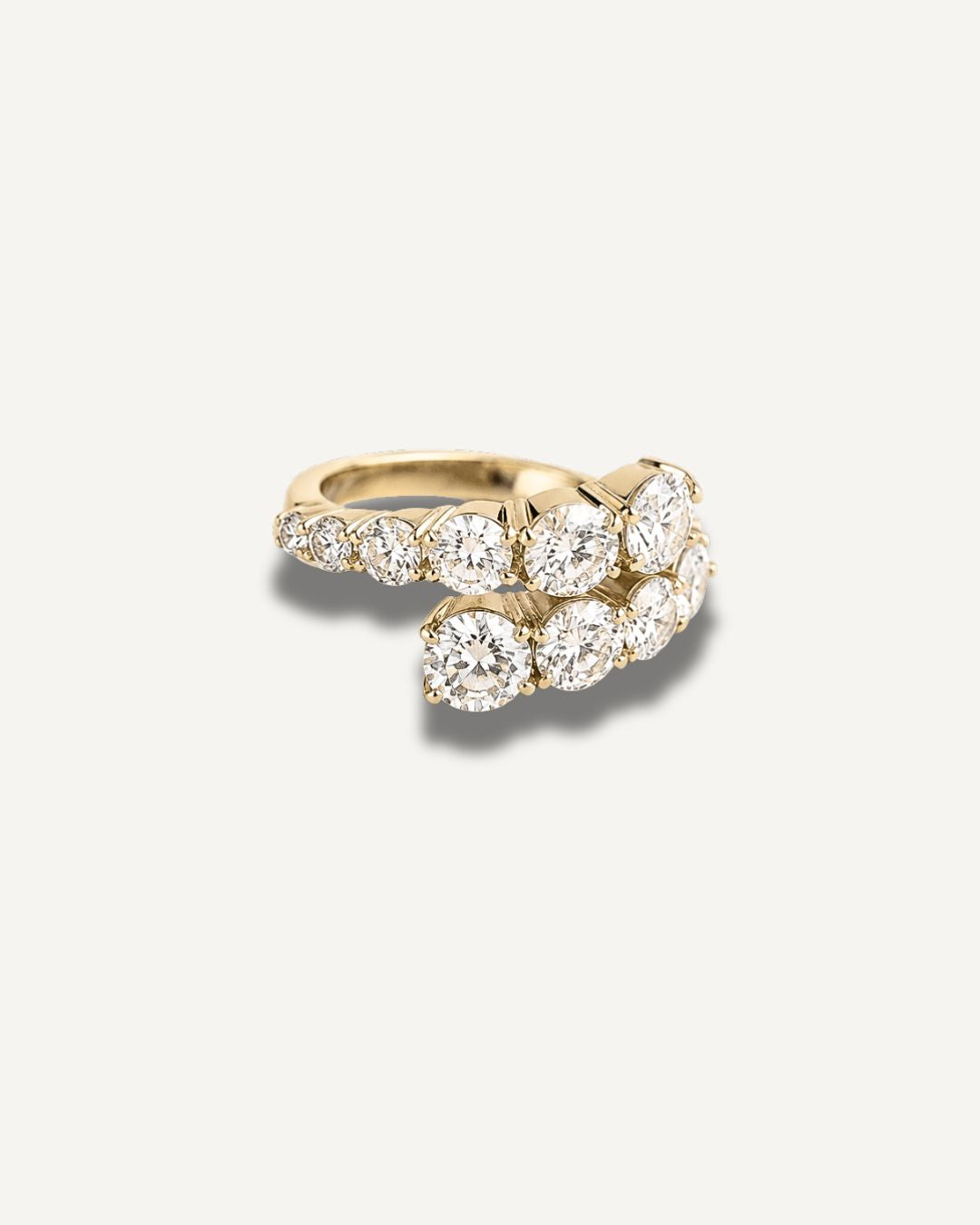 A gold wrap ring featuring a cluster of round-cut clear moissanite gemstones, photographed on a clean off-white background with a soft shadow.