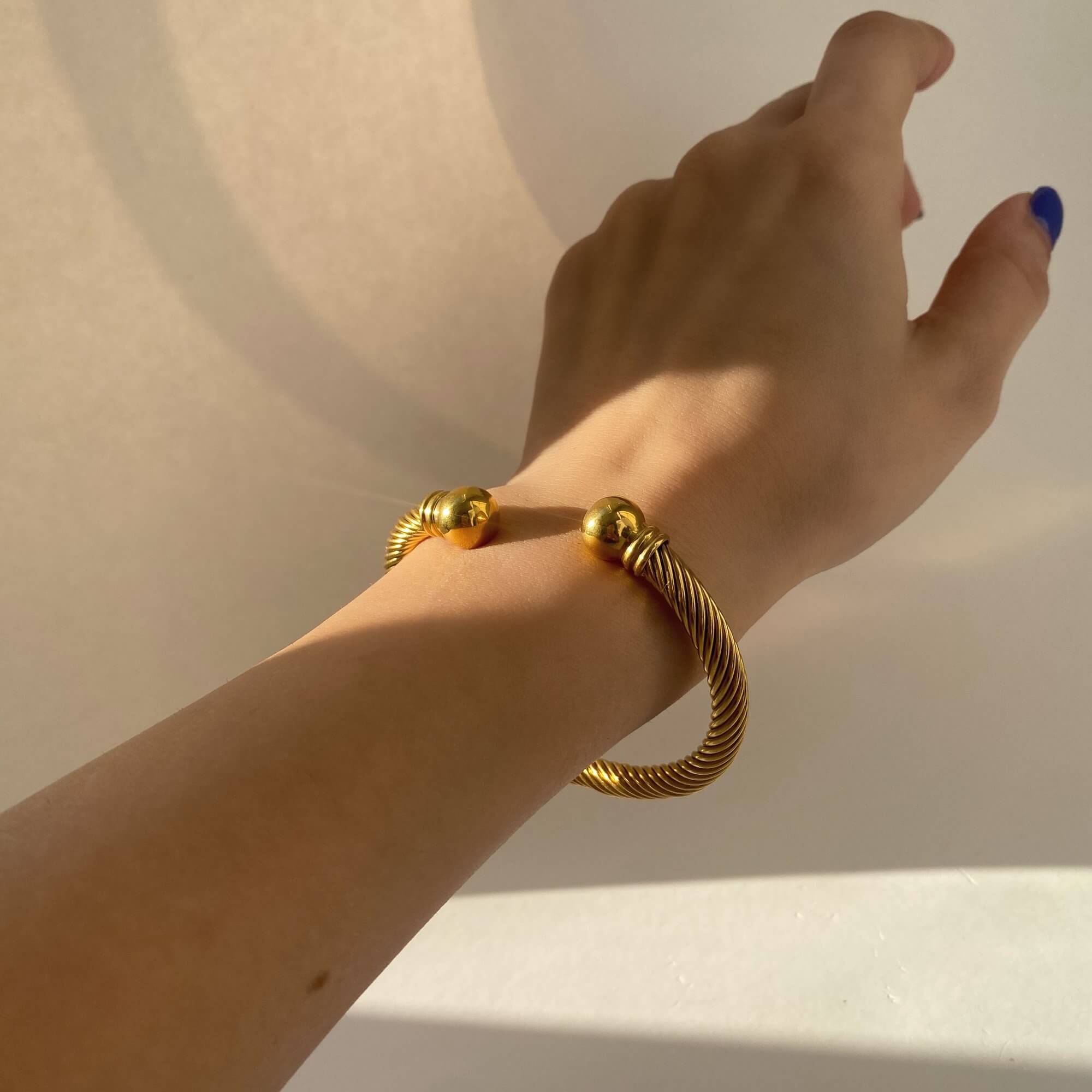 The KammyB gold twist cuff bracelet by Kampy Designs, worn on the wrist to highlight its elegant wraparound style and feminine silhouette.
