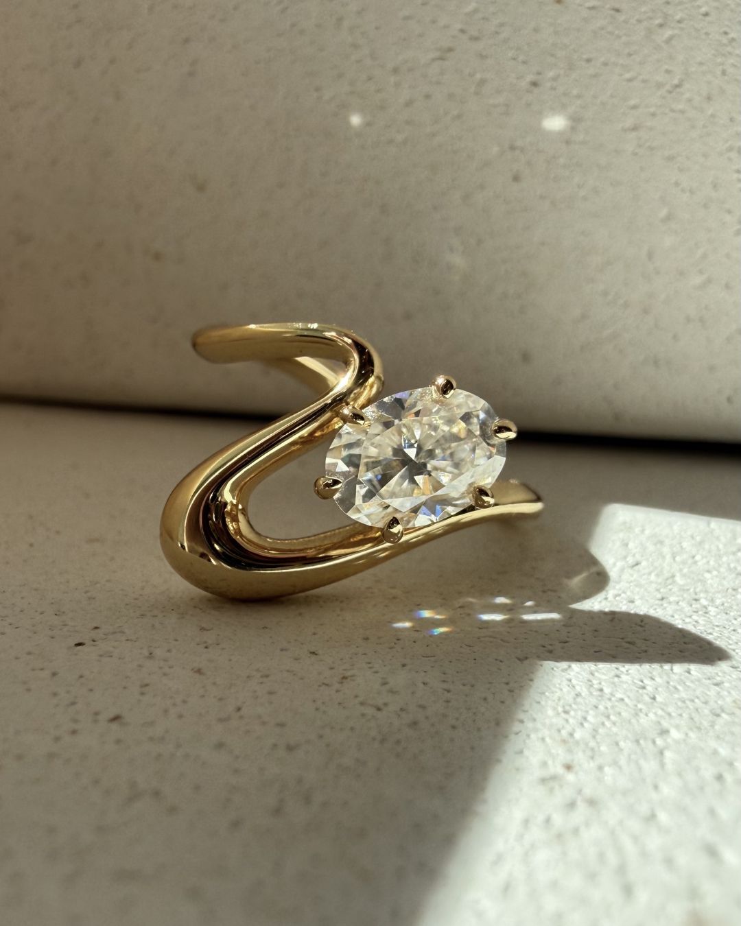 Minimal gold pinky ring with oval moissanite stone captured in soft natural light with subtle shadows