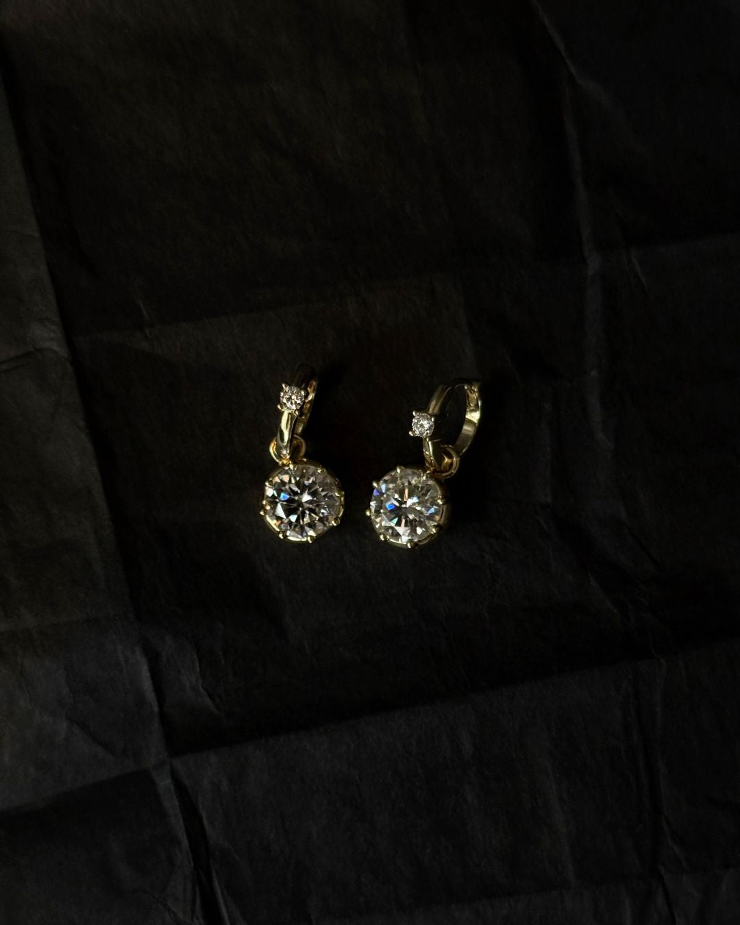 Gold drop earrings with gemstones on a black fabric background