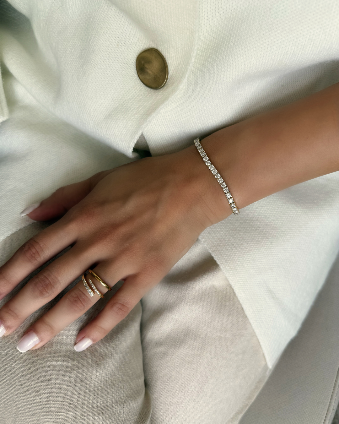 Hand wearing a gold ring and silver bracelet on a white fabric background