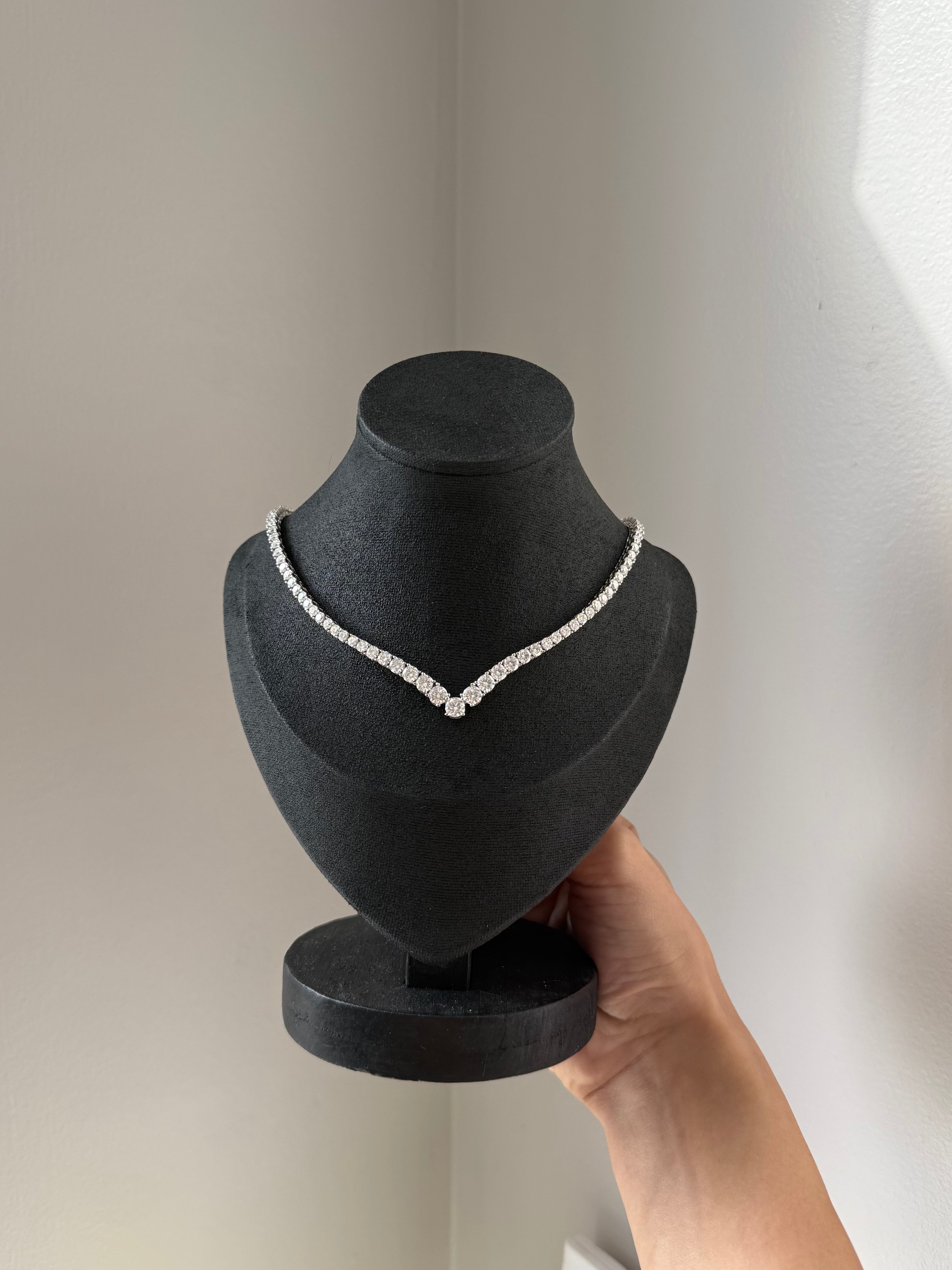 Moissanite necklace on a black bust display held by a hand against a neutral background
