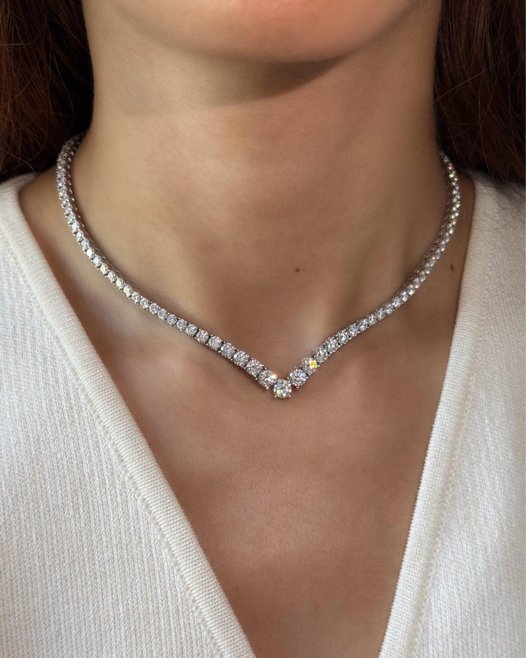 Close-up of a diamond necklace on a person wearing a white top.