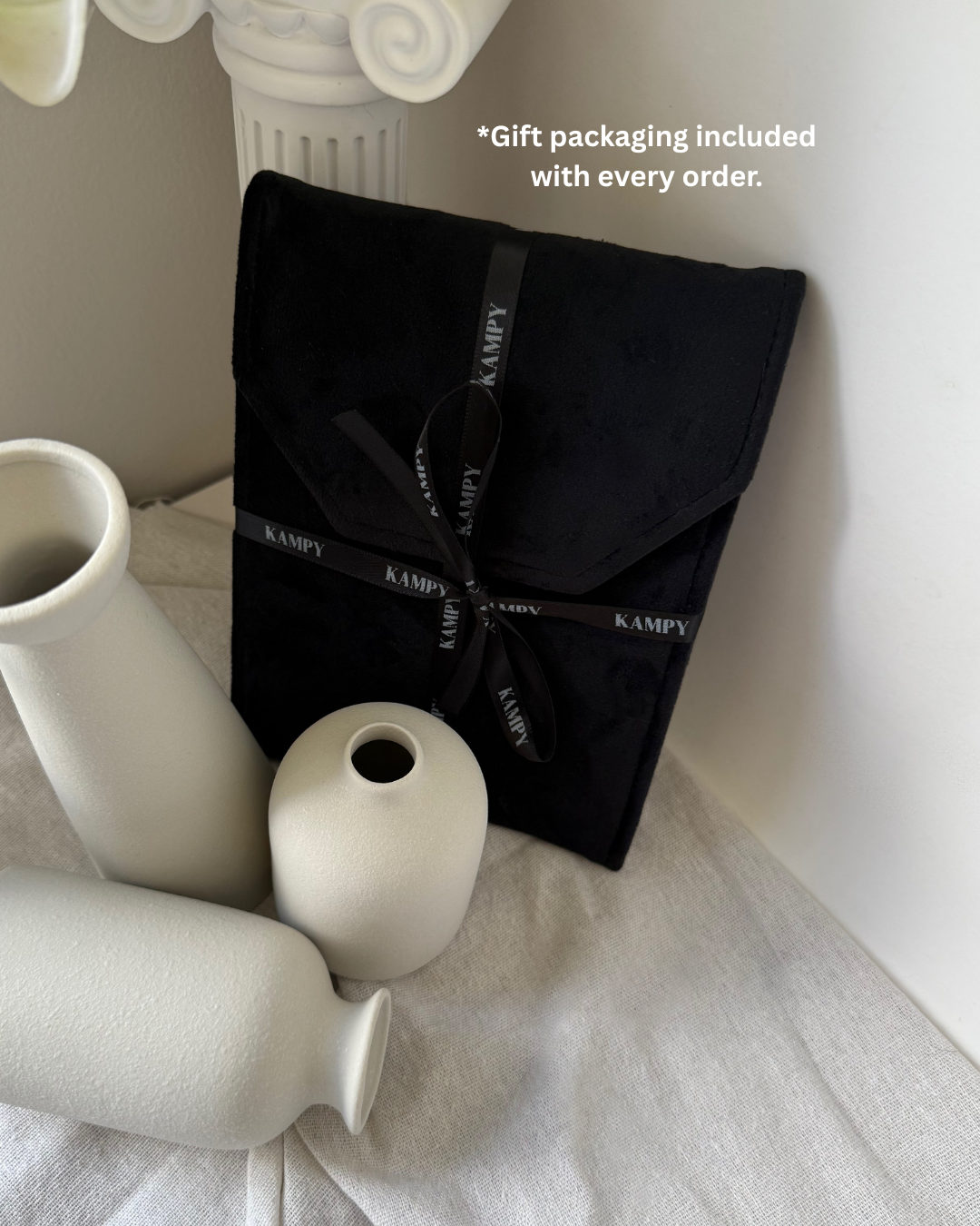 Black KAMPY gift packaging with white vases on a light surface