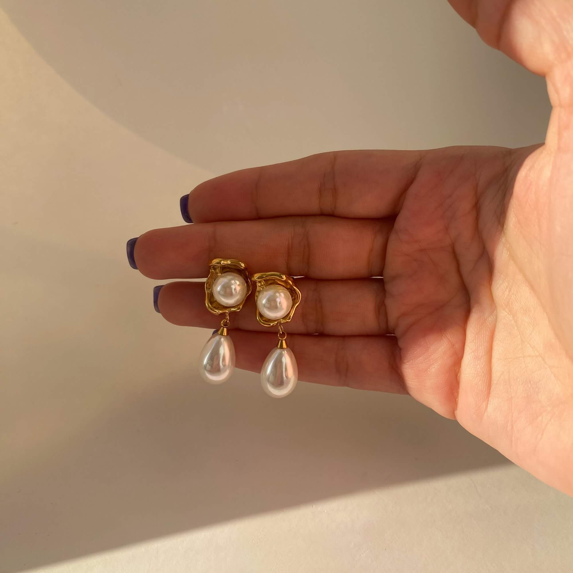 The KearyE oyster pearl dangle earrings by Kampy Designs, held by model to showcase the size and shimmering elegance of each piece.