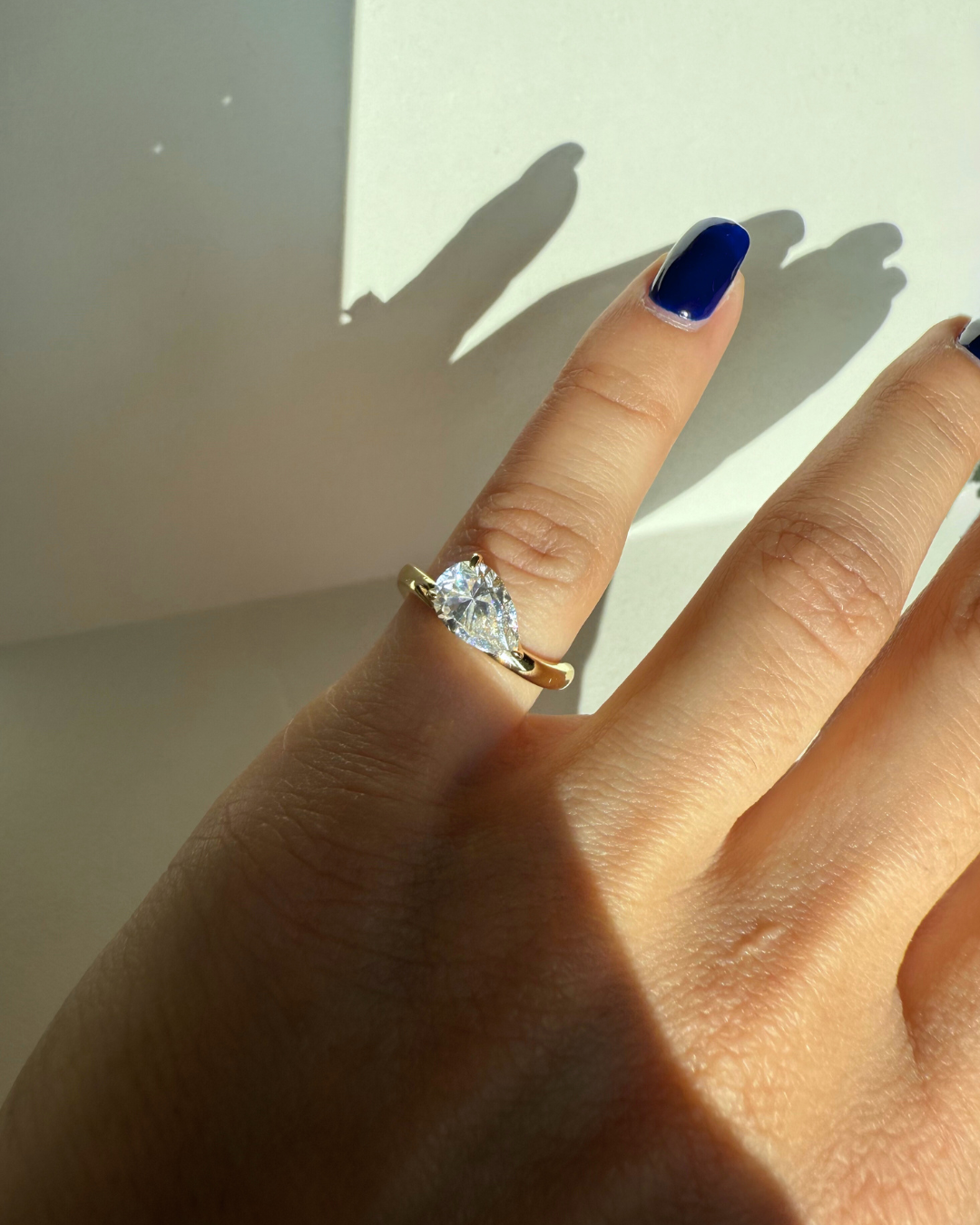 Close up of east-west pear cut moissanite wave ring worn on model pinky, Kampy Designs