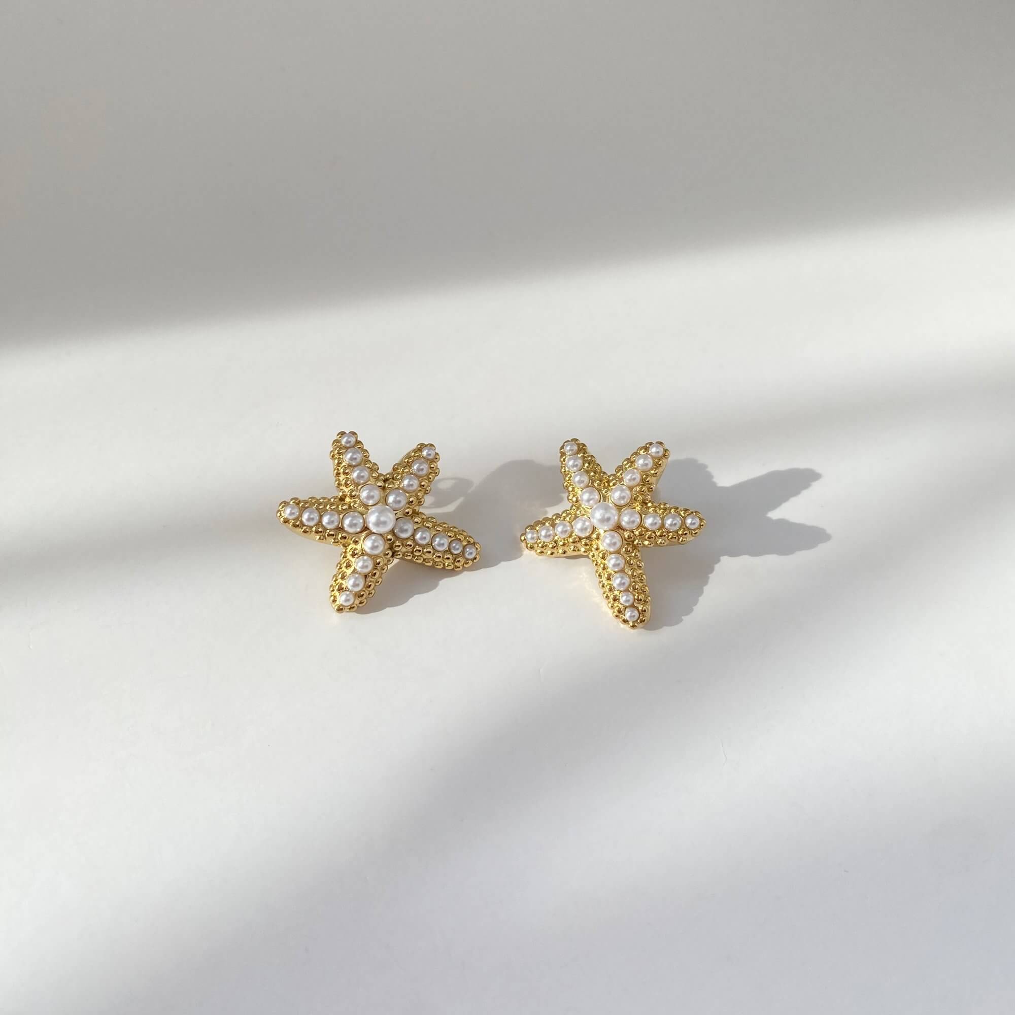 Flat lay of KeachyE pearl starfish earrings by Kampy Designs, arranged to showcase the star-shaped frame and lustrous pearl centerpieces.