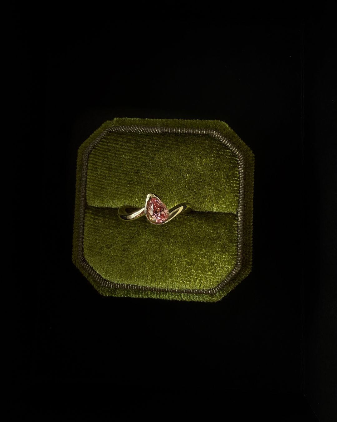 Pink sapphire ring displayed in a velvet jewelry box with a soft textured background