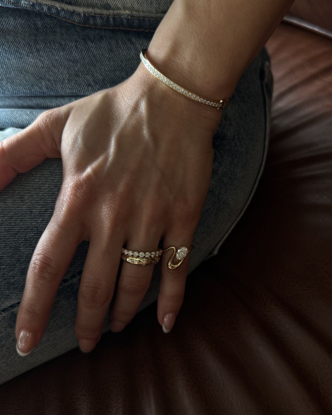 Gold oval moissanite pinky ring styled in a stacked ring look with complementary jewelry pieces