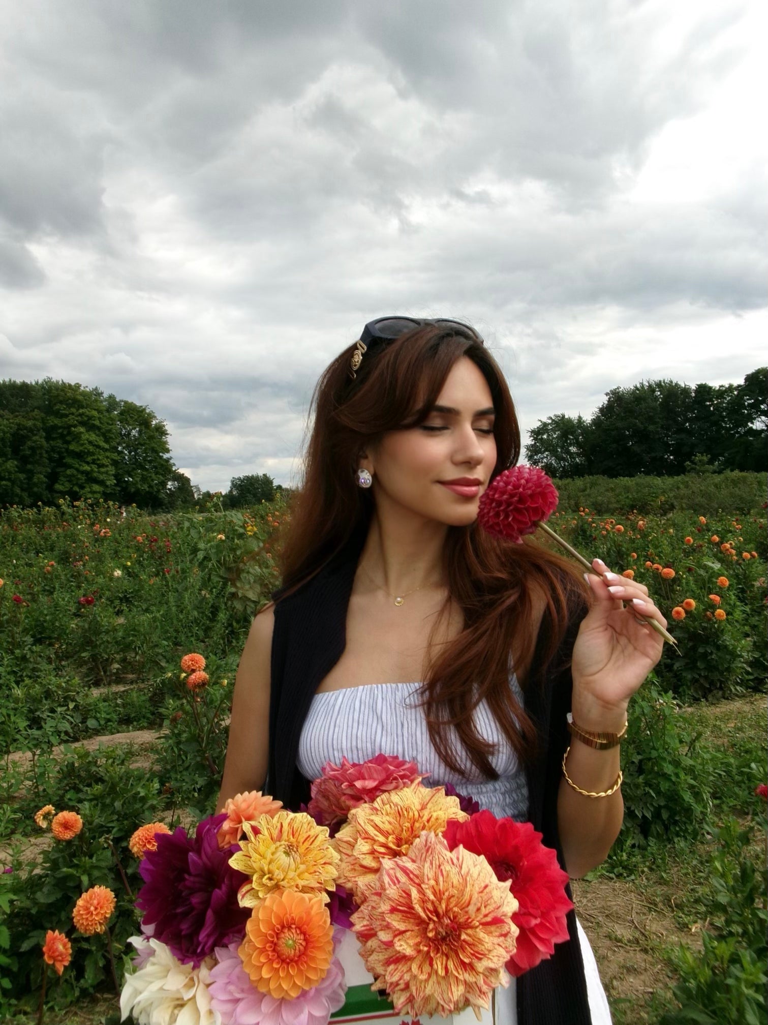 Sara Kampy holding a bouquet of flowers in a field with a cloudy sky.