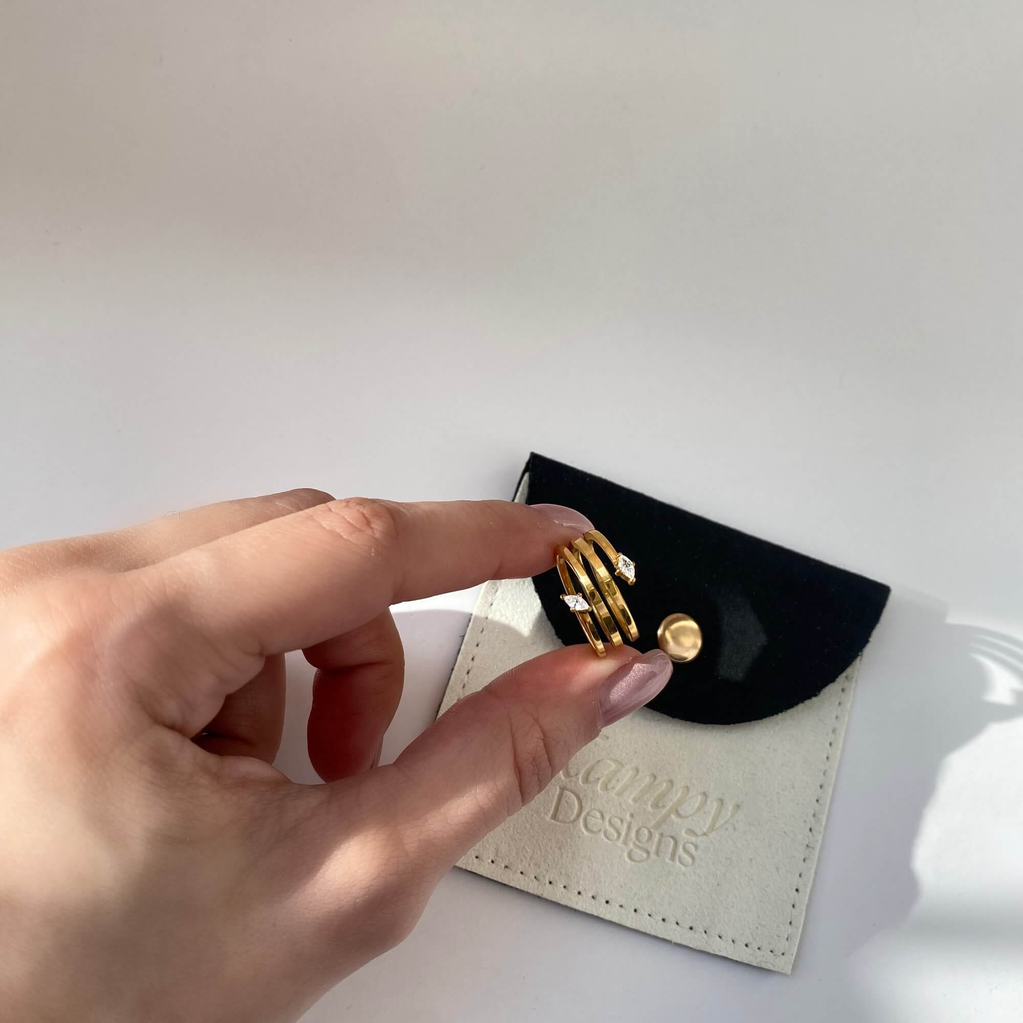 The Kinor serpentine wrap ring by Kampy Designs, held by model to showcase its detailed curves and wrap-around structure.