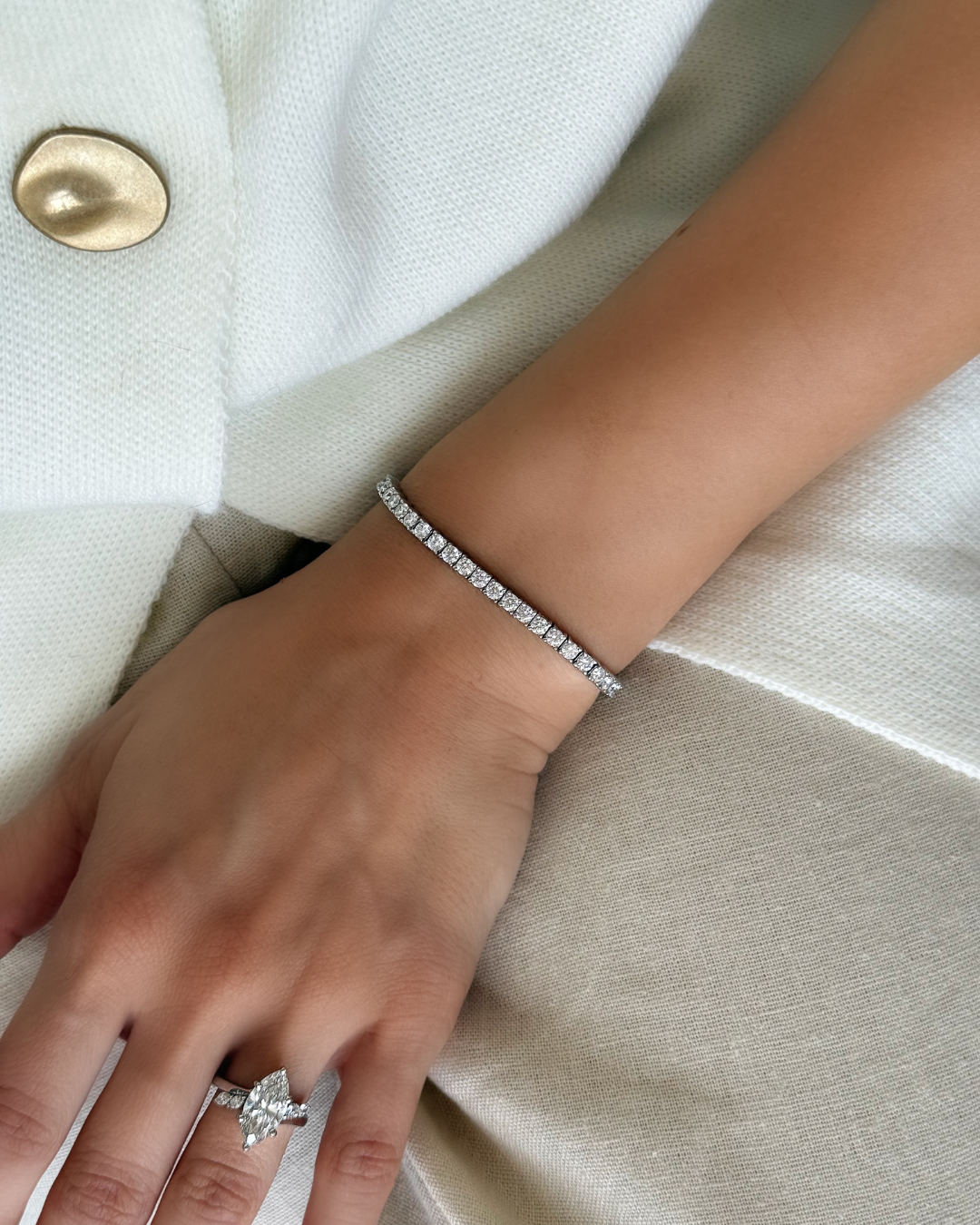Close-up of a hand wearing a diamond ring and bracelet on a light fabric background