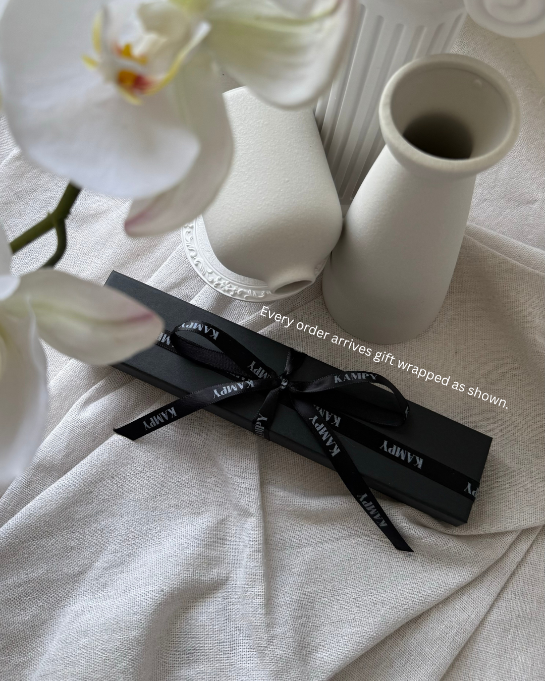 White orchids with a black ribbon and 'kampy' branding on a light surface.