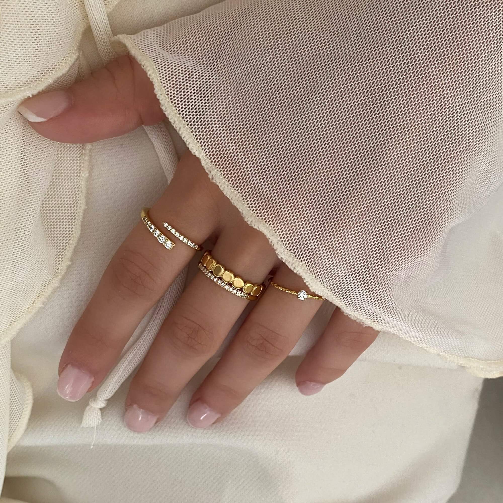 The KikoR thin diamond stacker ring by Kampy Designs, styled with other rings to highlight its classic diamond-studded gold band.