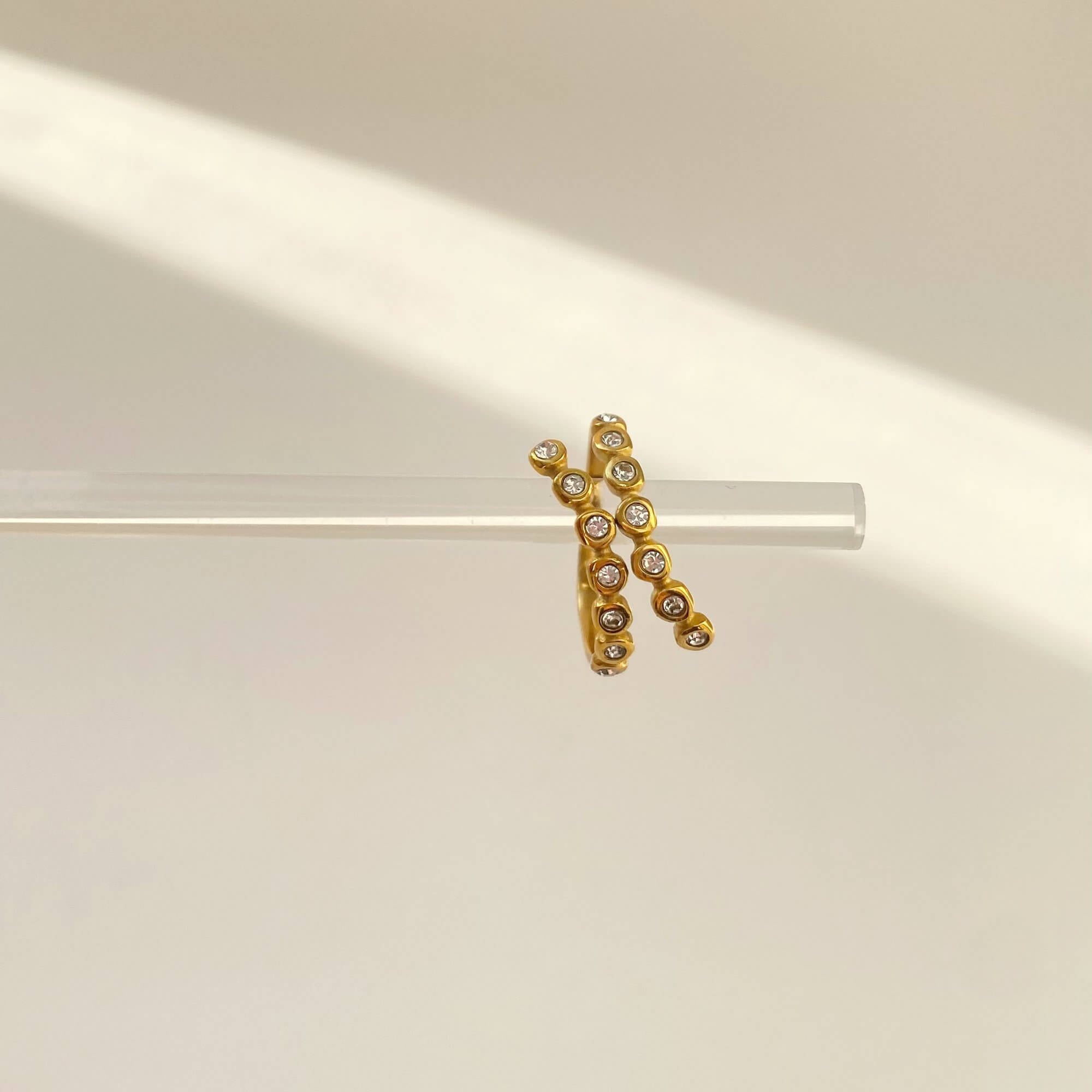 Dangle view of the KazzyR zircon bezel wrap ring by Kampy Designs, showcasing the fluid open band and floating zircon detail.