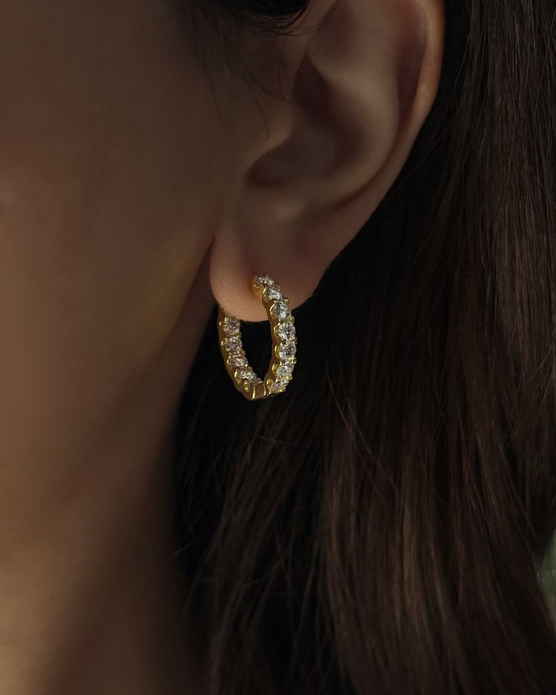 20 mm gold moissanite huggie earrings worn on ear, featuring round stones and 18k gold plating on 925 sterling silver.
