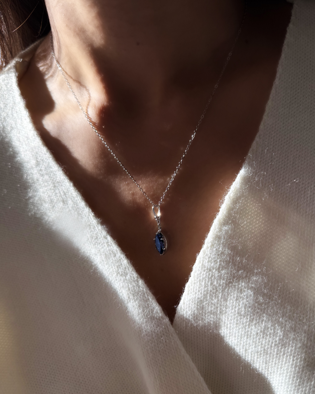 Midnight blue marquise moissanite pendant necklace worn on model in natural sunlight with silver chain.