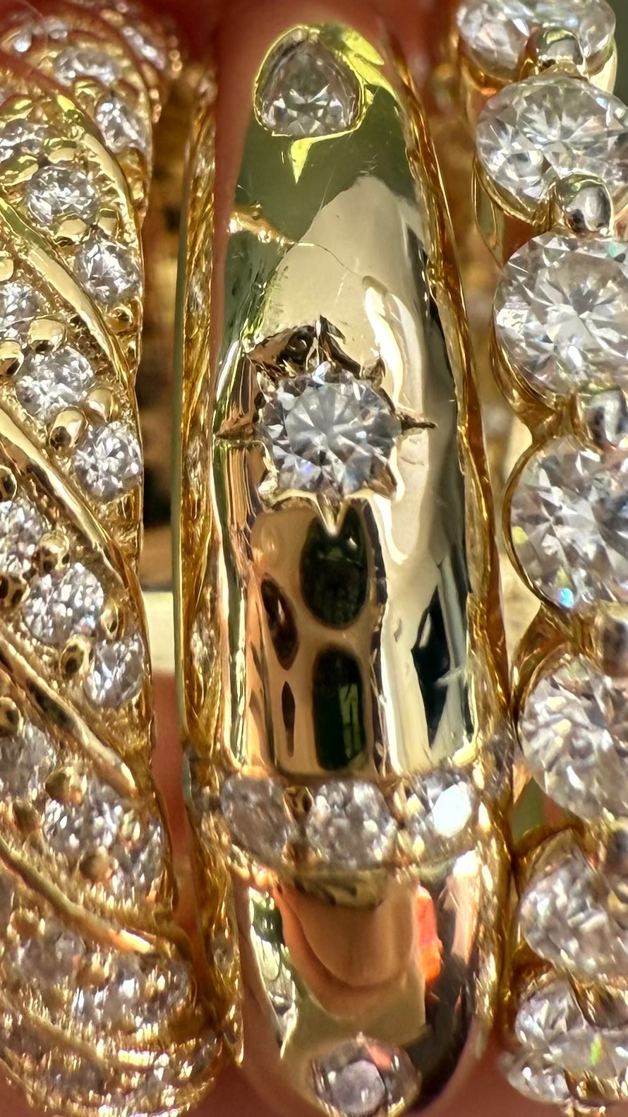 Three gold and moissanite rings being held between fingers against a blurred green background