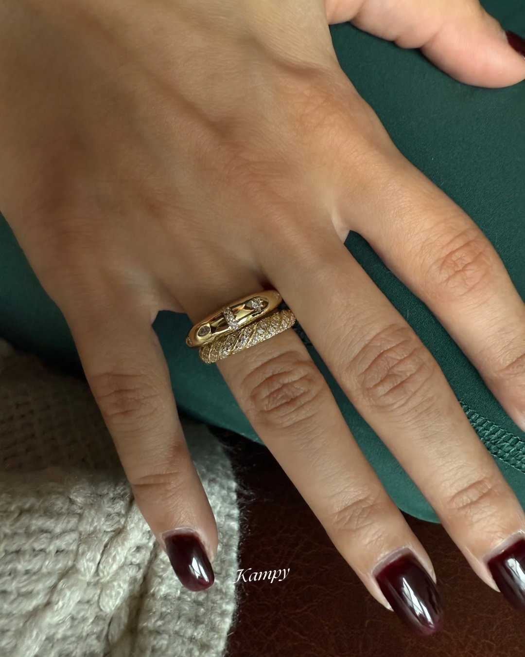 Hand wearing a gold ring with a twist pave band design stacked with a gold dome ring with moissanite accents 
