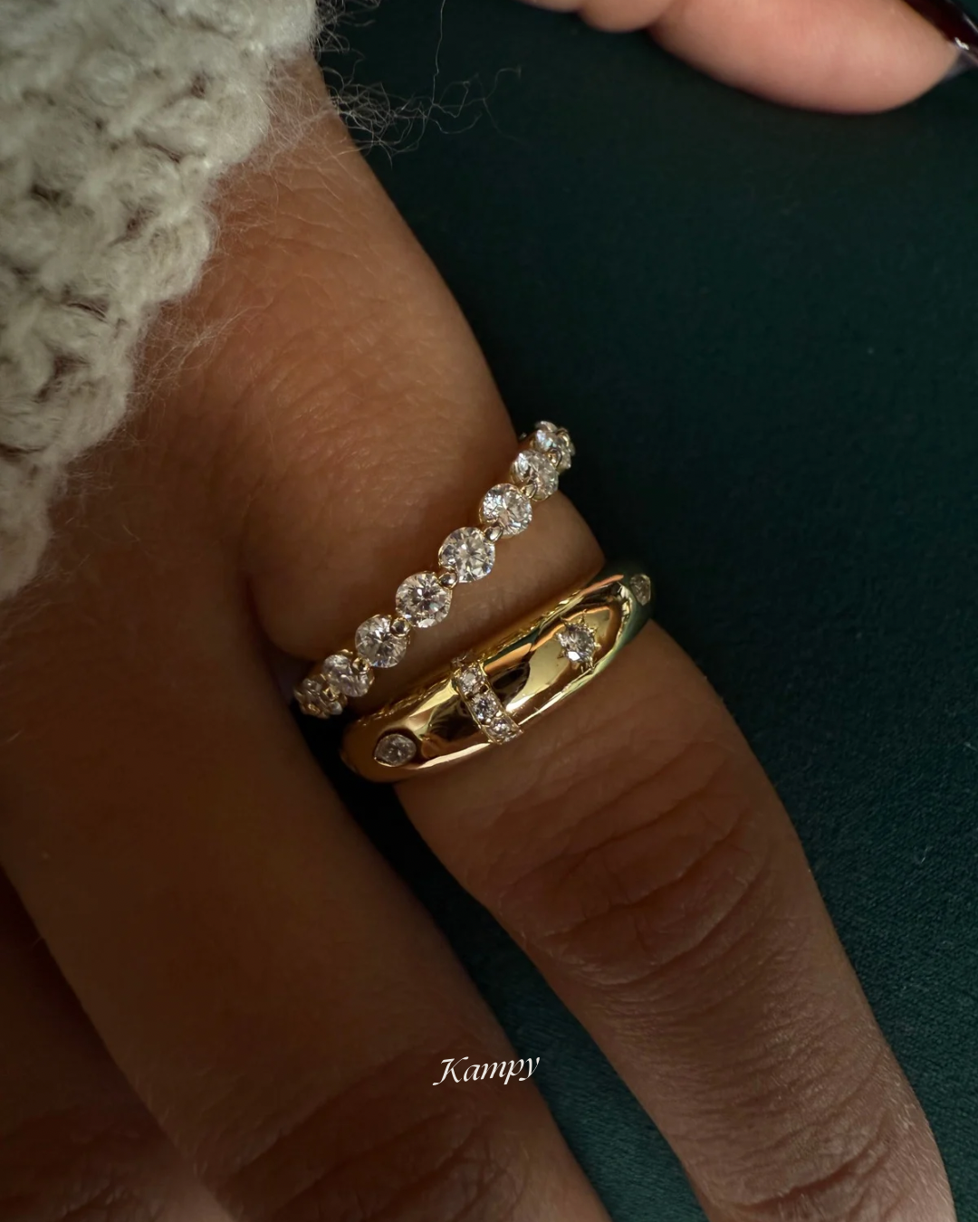 Close-up of a hand wearing two moissanite rings by Kampy on a dark background