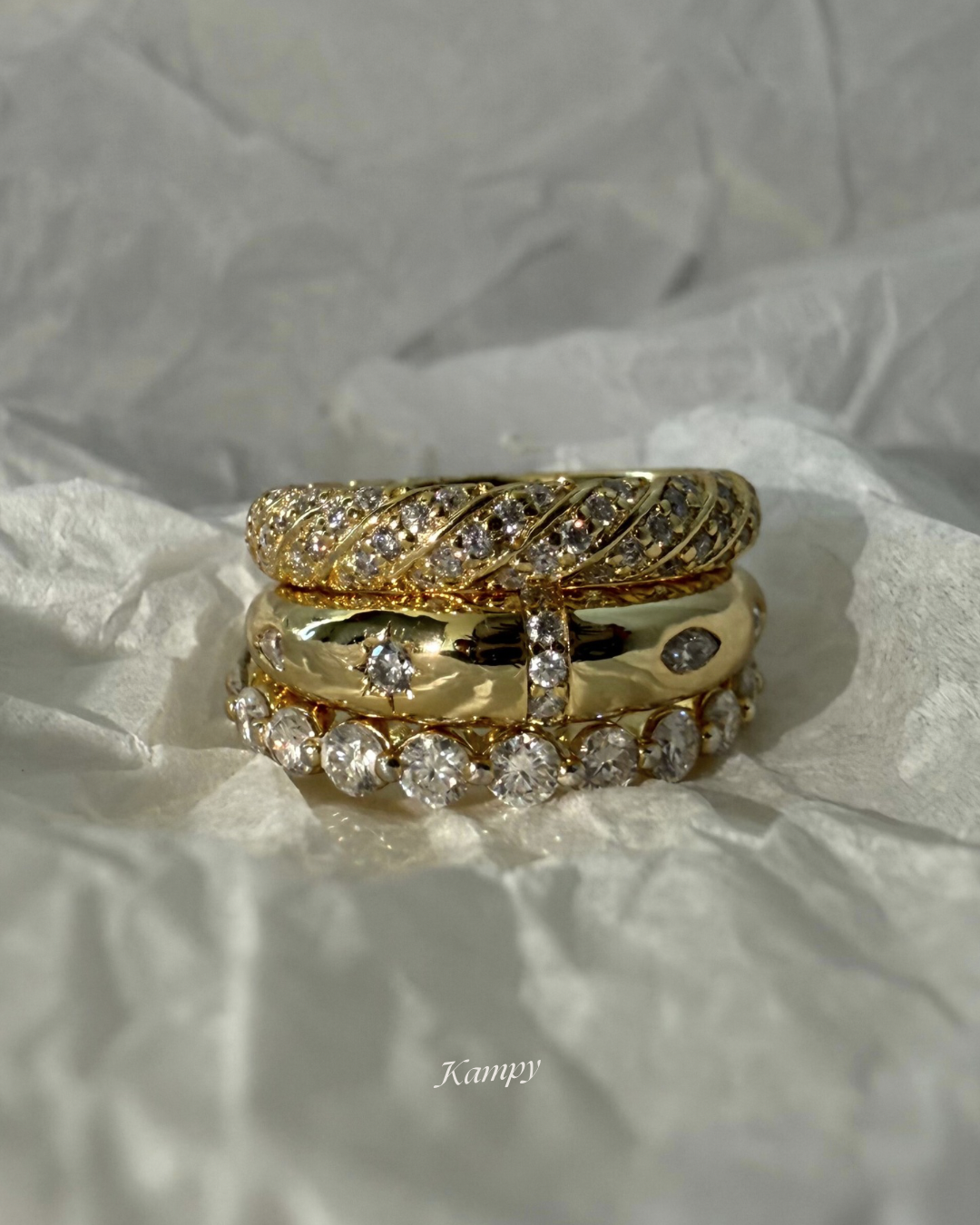 Three gold rings with moissanite stone accents stacked on a white fabric background