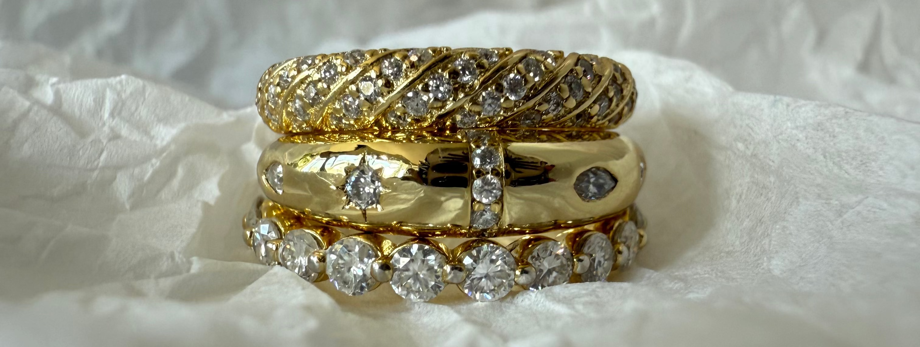 Stack of gold and diamond rings on a textured white surface
