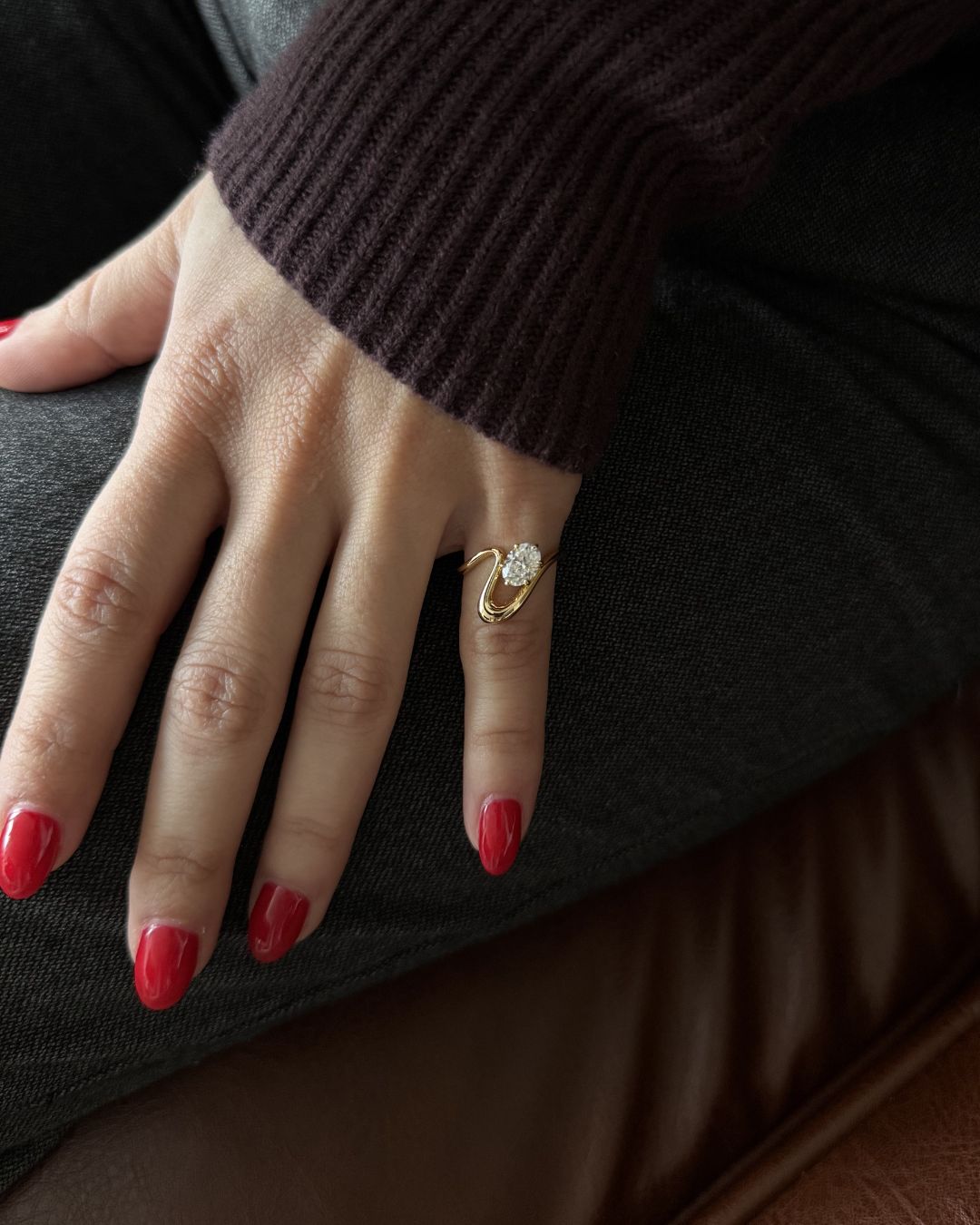 Gold oval moissanite pinky ring styled with glossy red nails in a close-up fashion shot