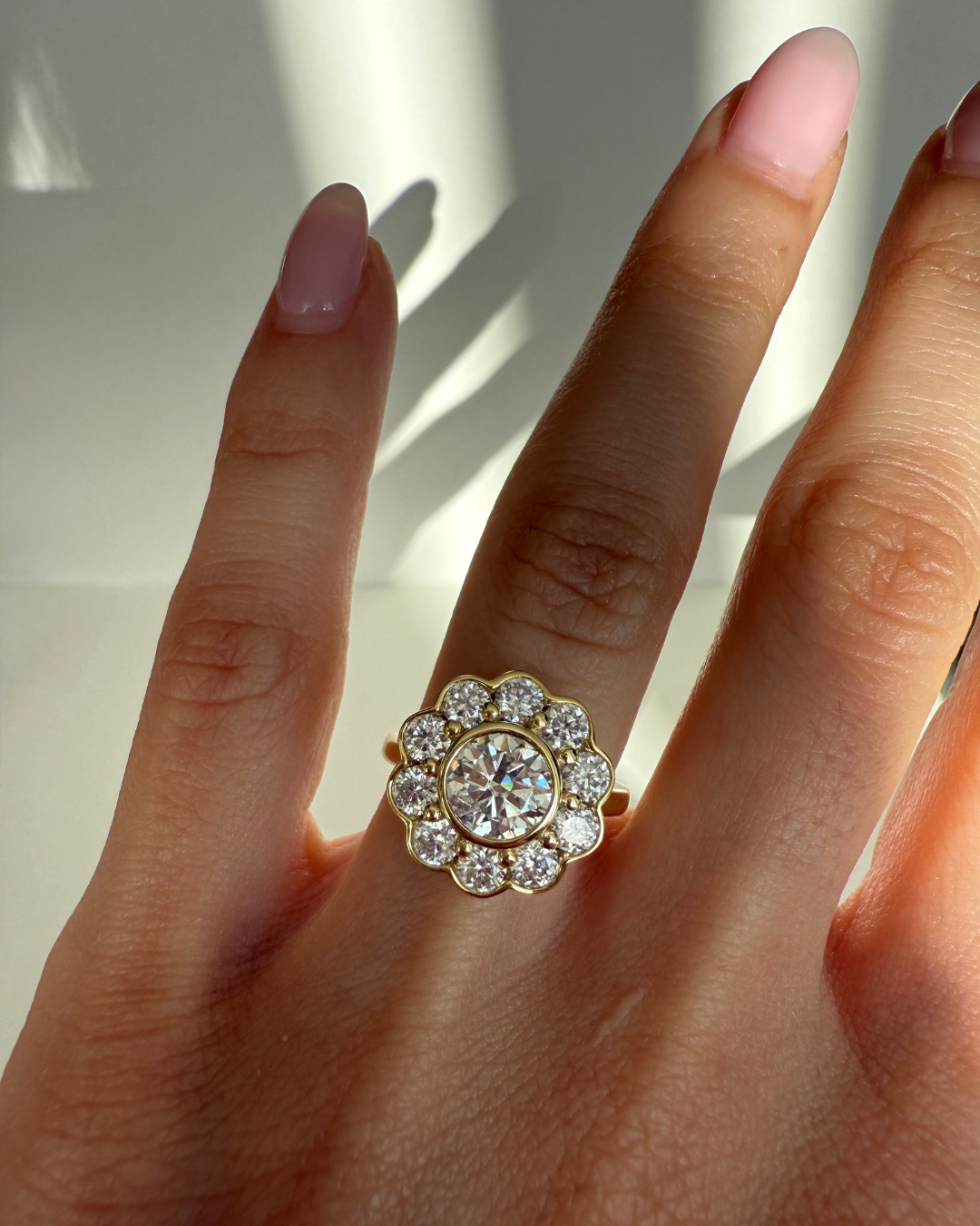 Close-up of The Marigold Ring in gold from Kampy Designs worn on a model’s finger, highlighting the bezel-set 1ct moissanite center and ten surrounding halo stones.