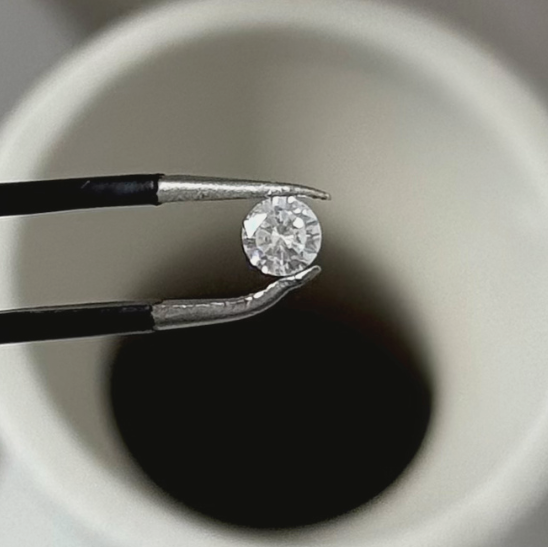 Moissanite held between tweezers against a neutral background