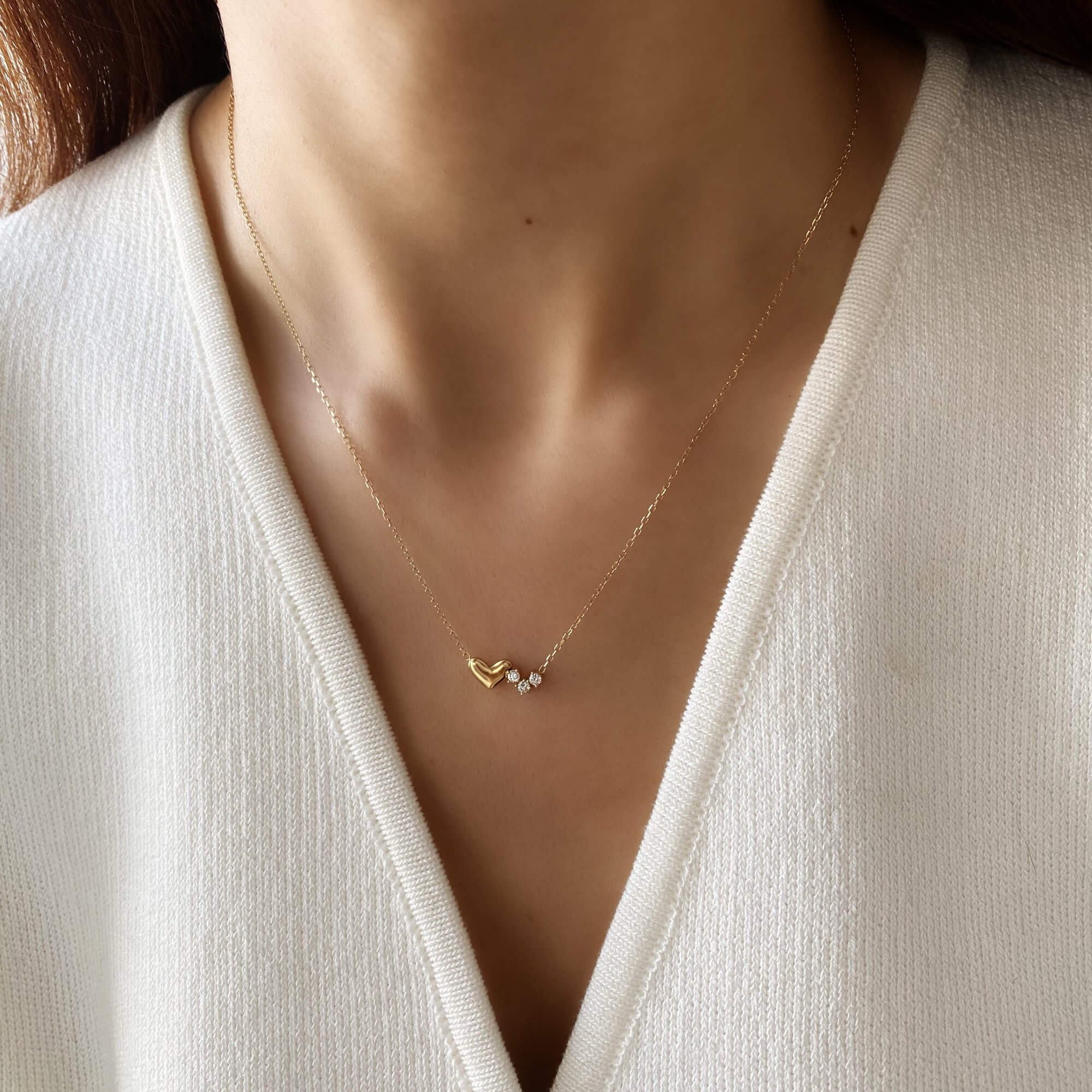 Angled view of the KassyN double heart charm necklace by Kampy Designs, showcasing its intertwined heart pendants and polished gold finish.