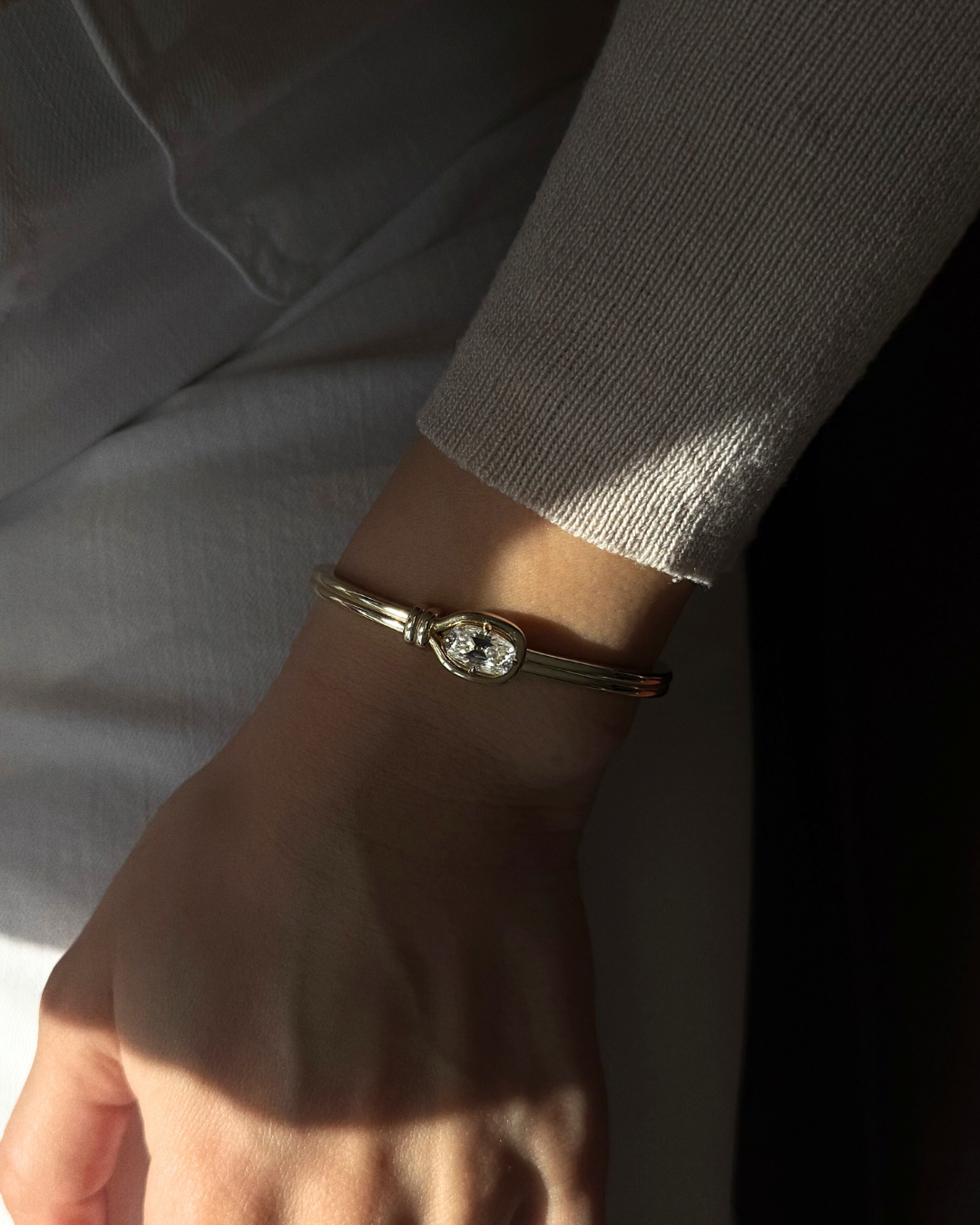 Elara 2ct elongated cushion moissanite knot bangle in 14K gold worn alone on wrist in soft natural light, luxury statement bracelet.
