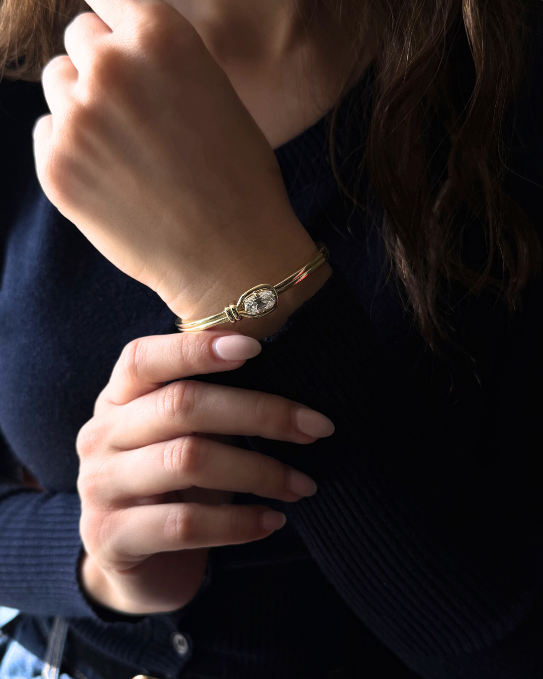 Close up of Elara moissanite knot bangle worn on wrist in 14K gold featuring elongated cushion cut center stone, modern statement bracelet styling.