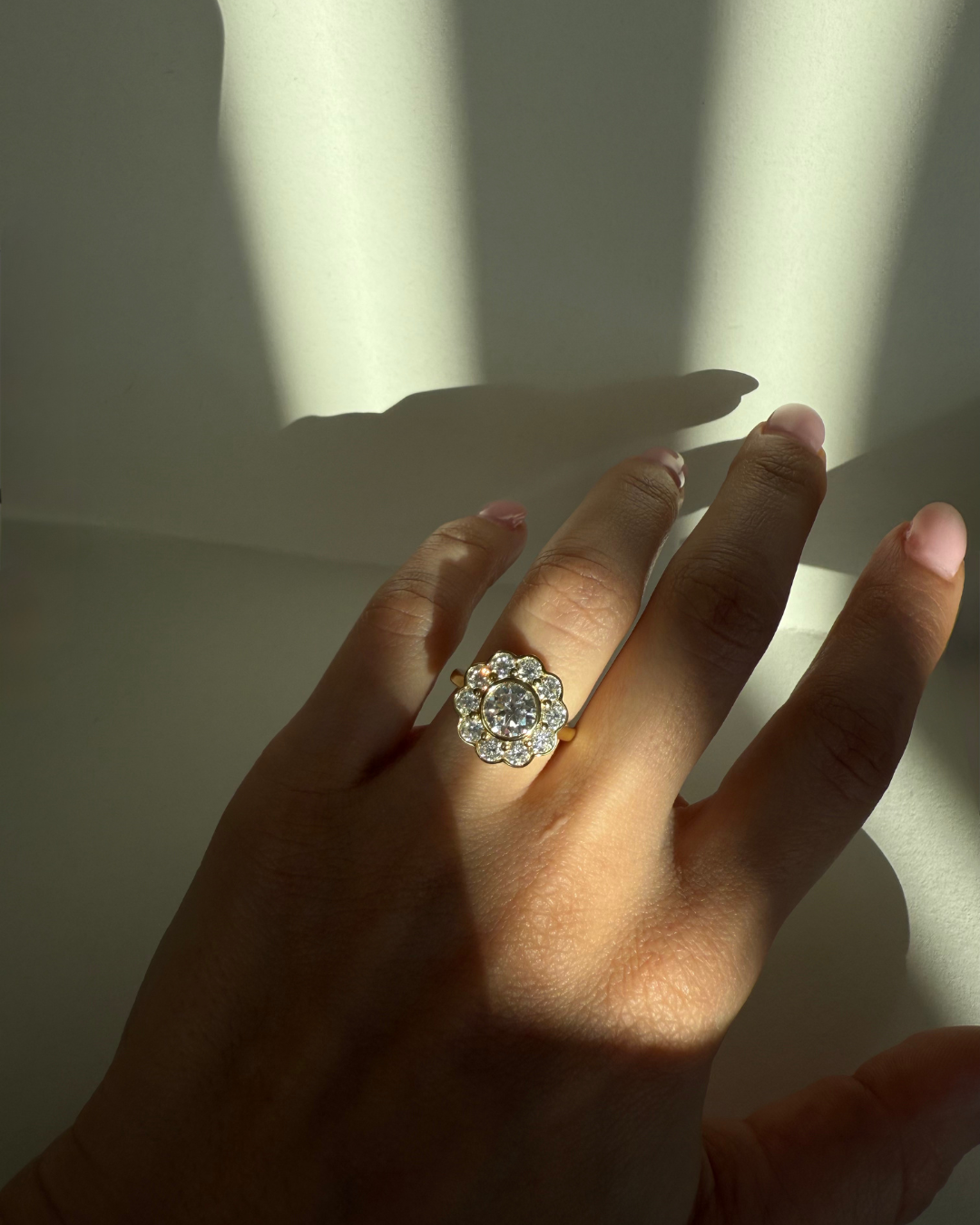 Close-up of The Marigold Ring in gold from Kampy Designs worn on a model’s finger, highlighting the bezel-set 1ct moissanite center and ten surrounding halo stones.