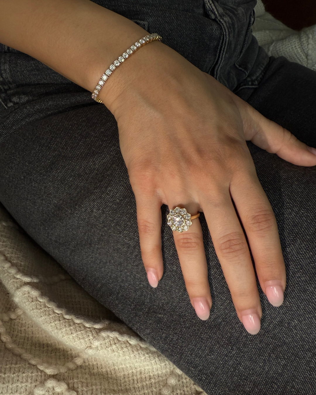 Lifestyle photo of The Marigold Ring in gold from Kampy Designs worn on a model’s hand resting on denim, showing the floral halo moissanite ring in everyday wear.