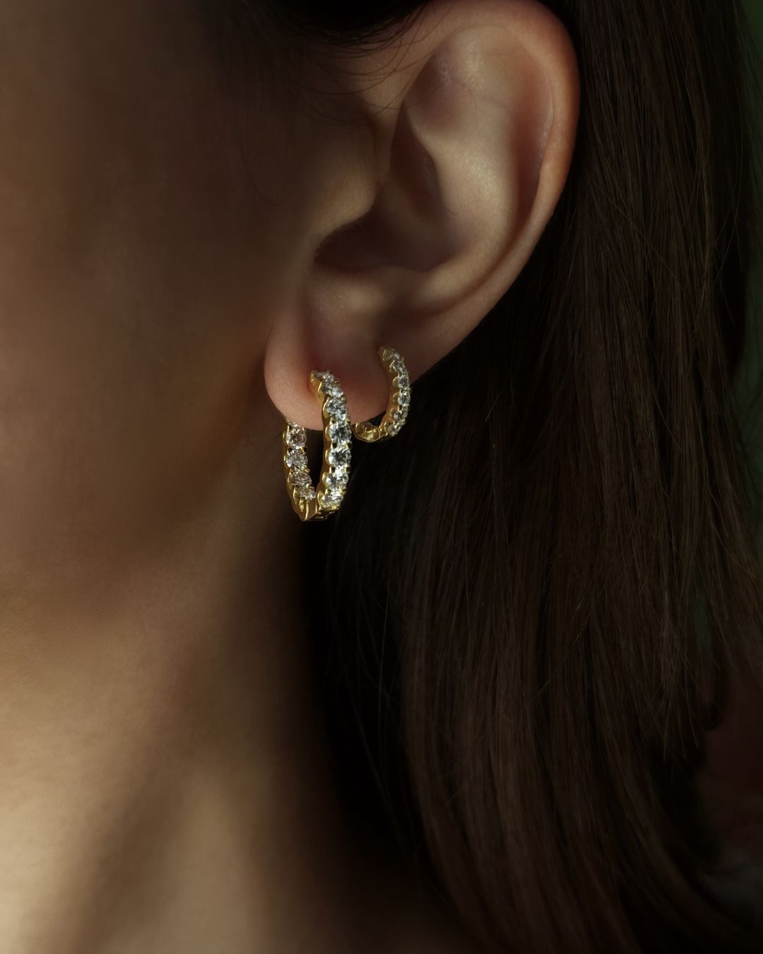Gold moissanite huggie hoop earrings shown on ear with sparkling stones and 18k gold plating on 925 sterling silver.