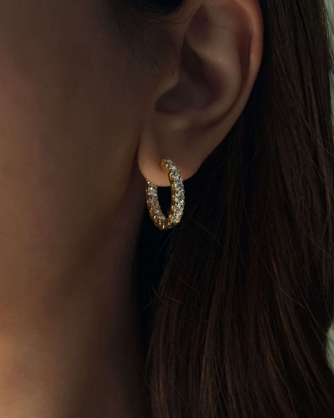 Close-up of gold moissanite huggie hoop earrings worn on ear with 20 mm hoop shape and brilliant round stones.