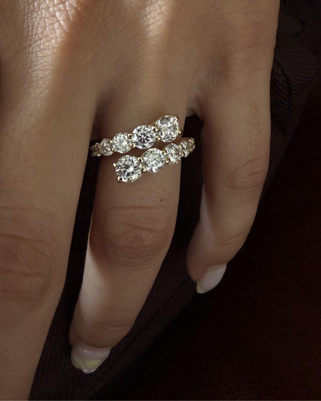 Close-up of a gold moissanite open wrap ring with graduated round stones.