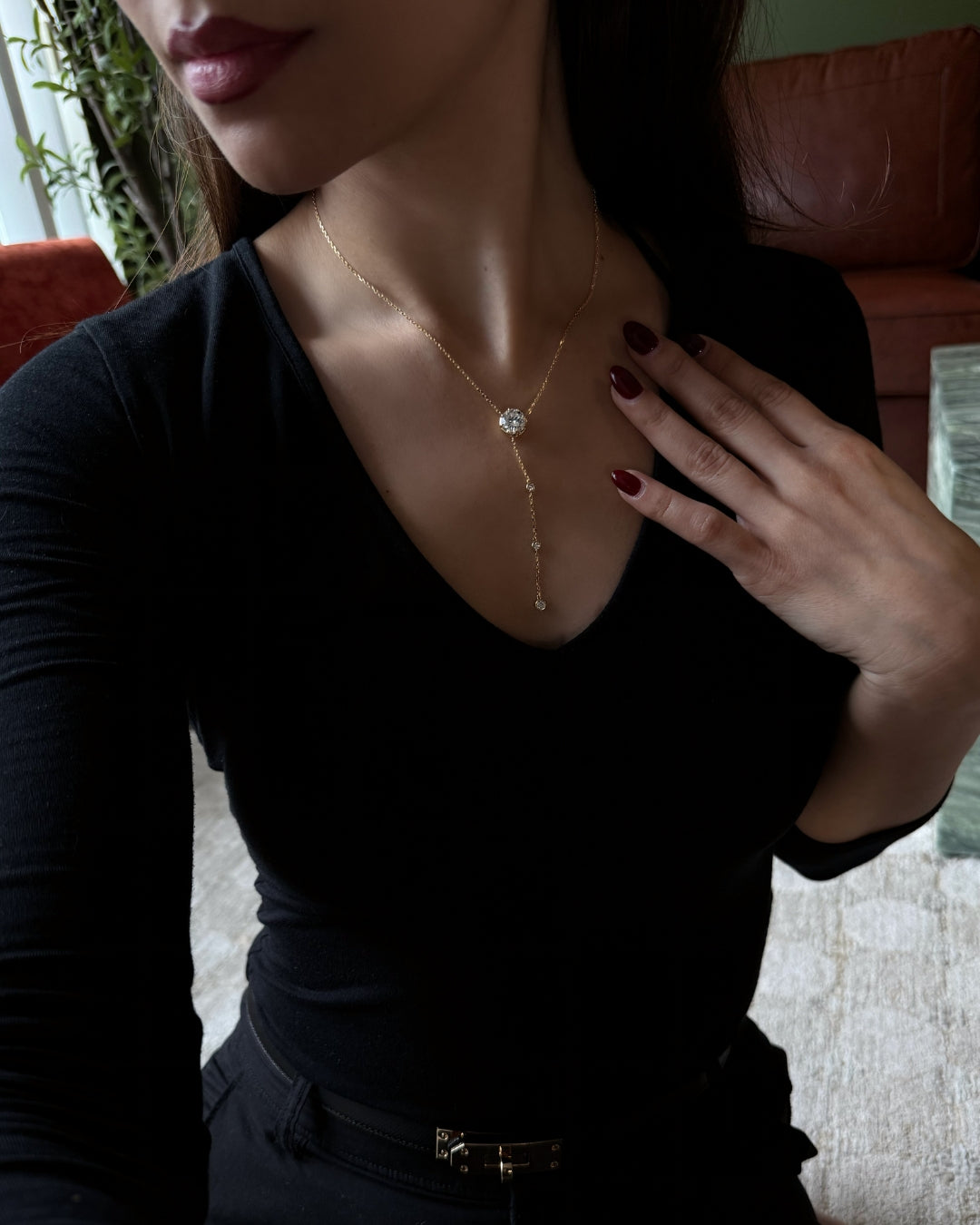A woman wearing a delicate gold Y-shaped sterling silver necklace by Kampy Designs with a central 3CT moissanite clear gemstone and a dangling bezel gems, styled with a black V-neck top.