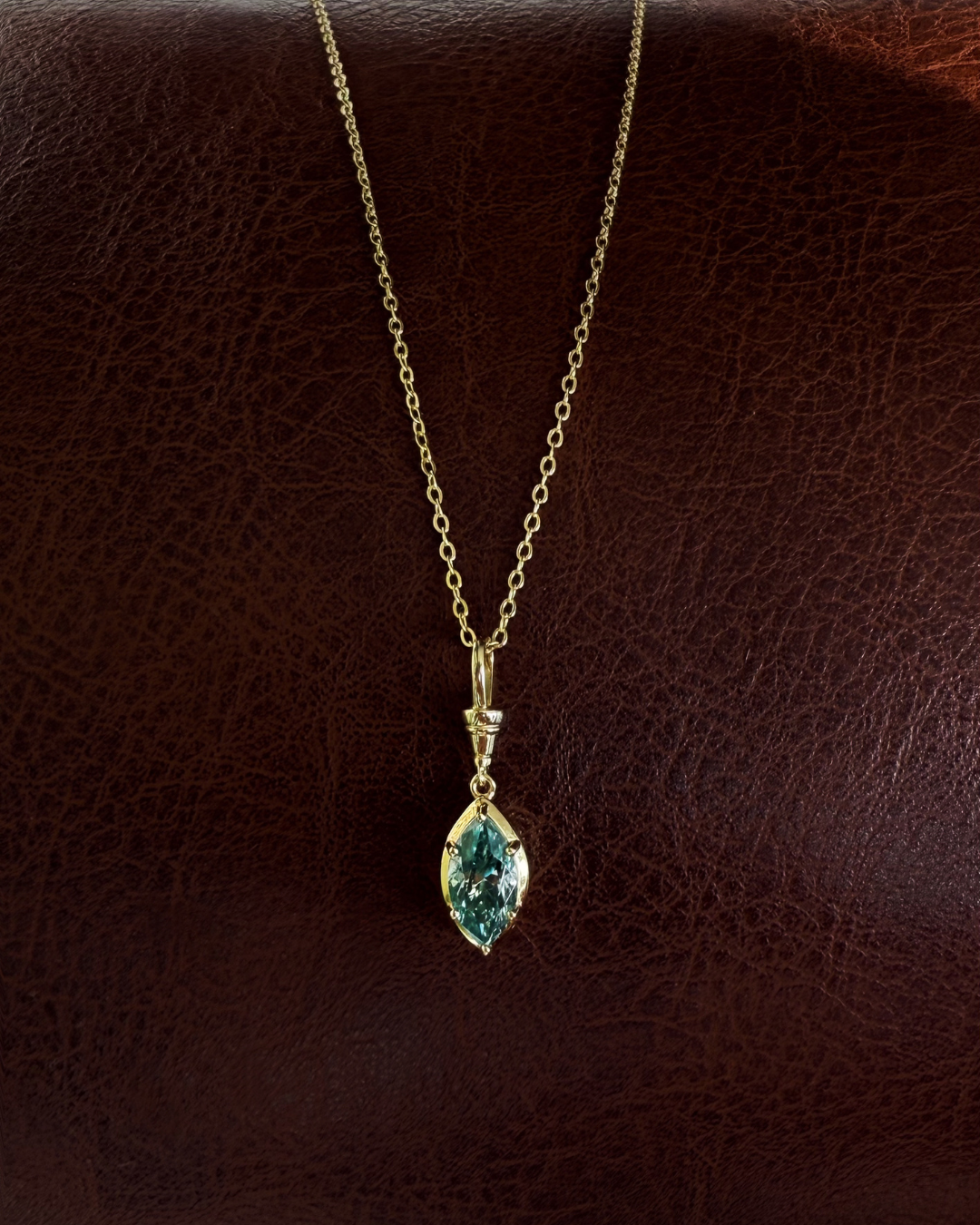 Green marquise moissanite pendant necklace on gold chain photographed on brown leather background by Kampy.