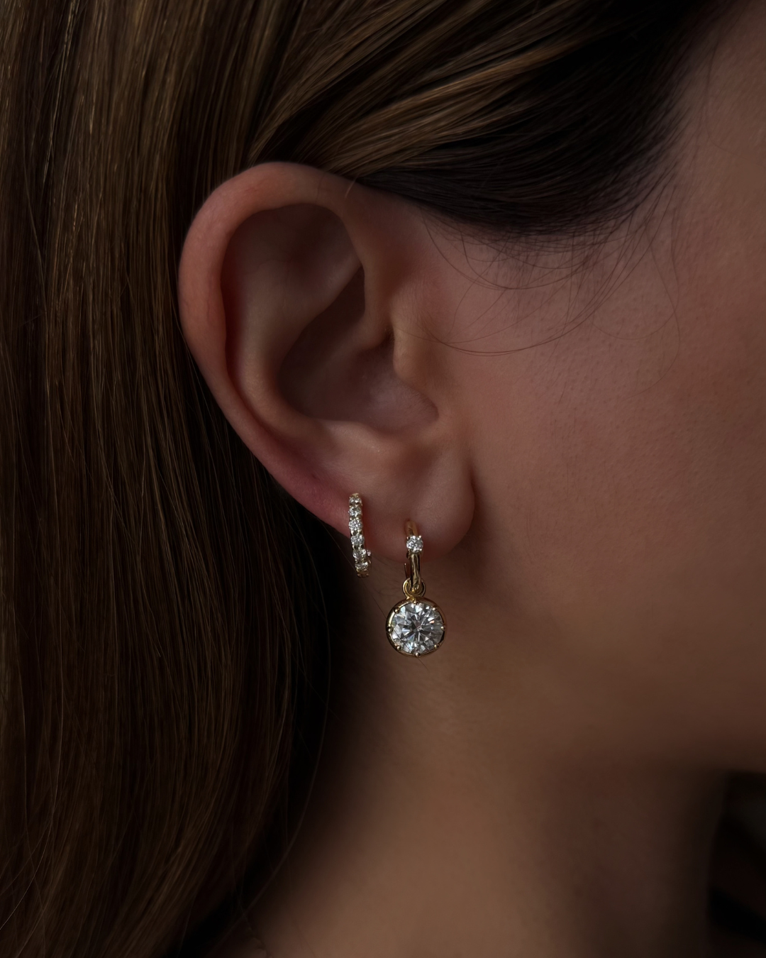 Kampy Designs Lumina Drop Earrings worn on ear, showcasing 2ct round-cut moissanite drop with gold huggie hoop.