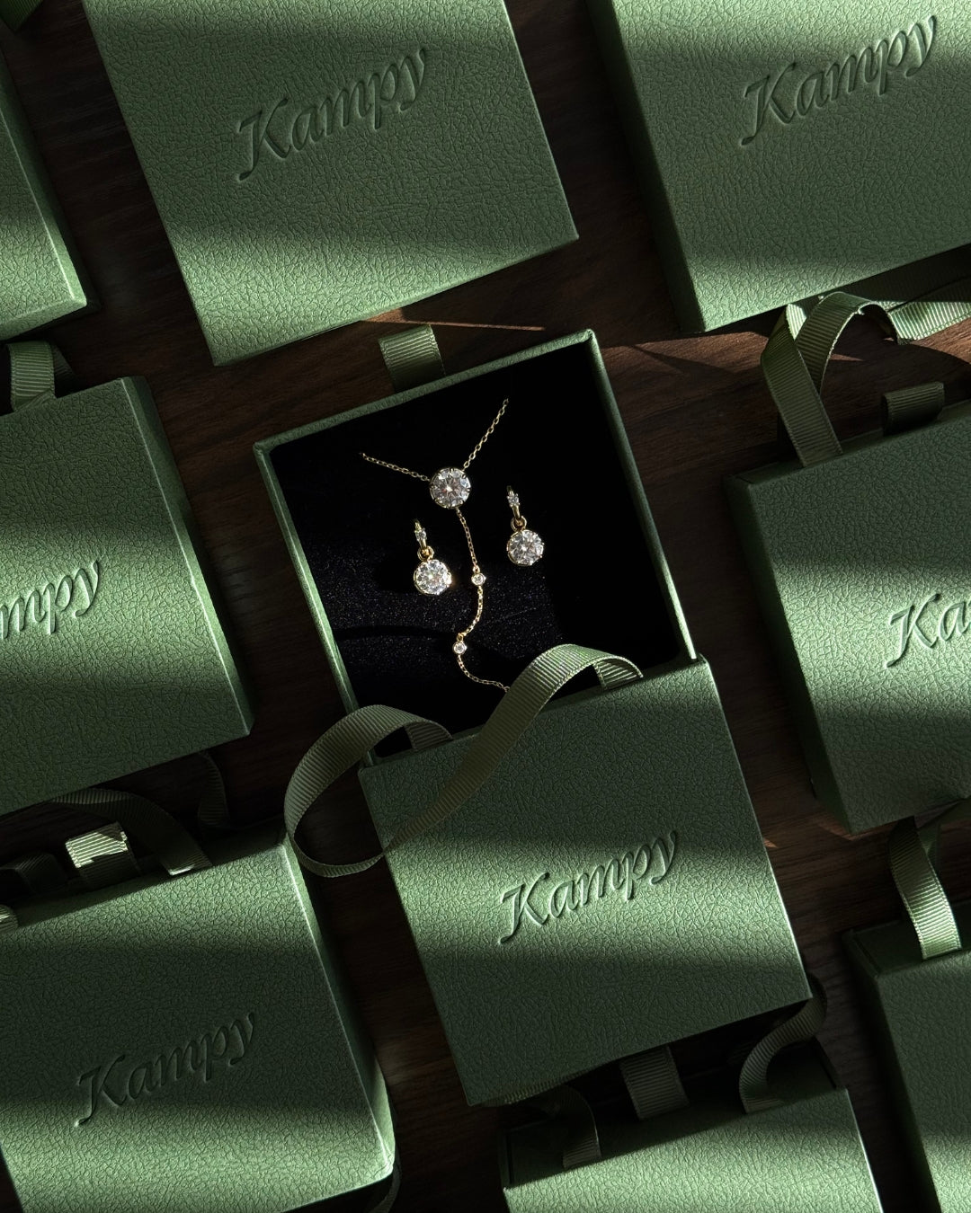 A gold-toned jewelry gift set with a necklace and matching earrings displayed in Kampy Designs' signature green gift box,  on a dark wooden surface.